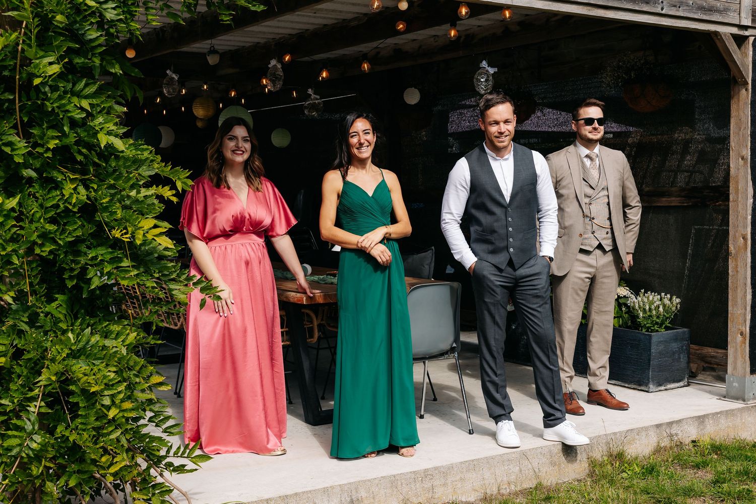 Wedding party poses outdoors, two bridesmaids in pink and green gowns with two groomsmen.