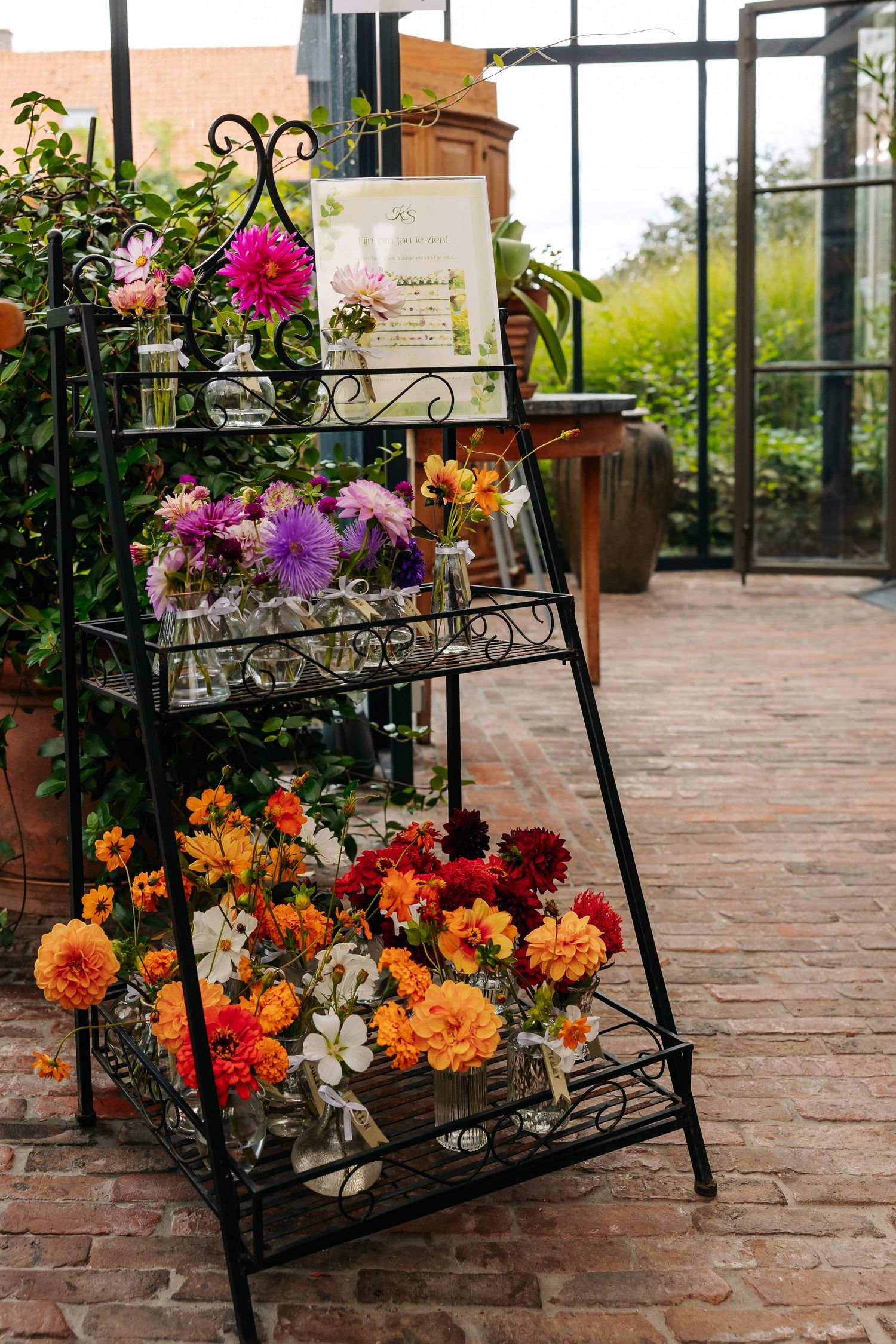 Colorful dahlia flower display on black metal tiered stand at wedding venue.