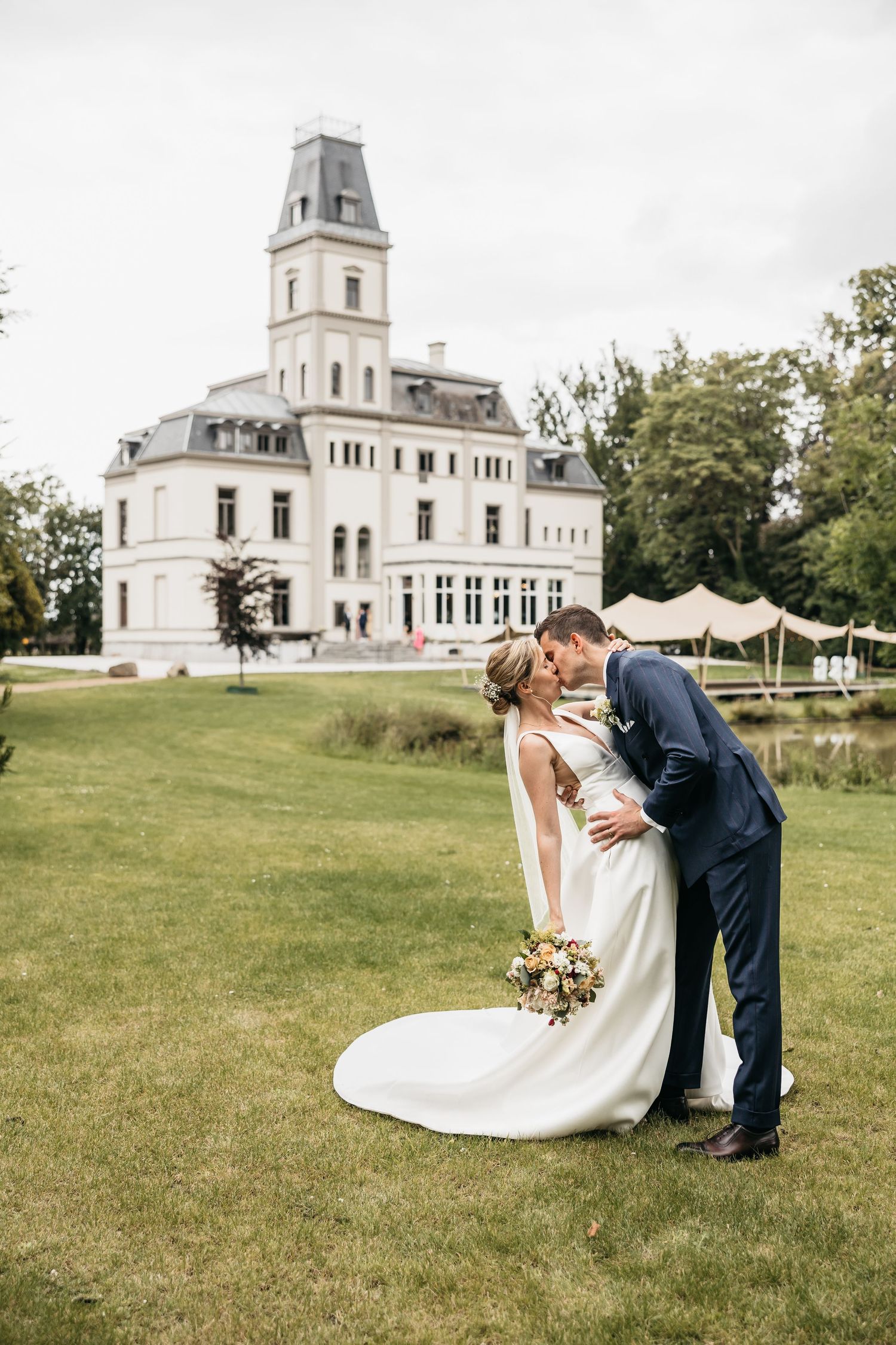Bride and groom sharing a romantic dip kiss on the lawn of an elegant white chateau.