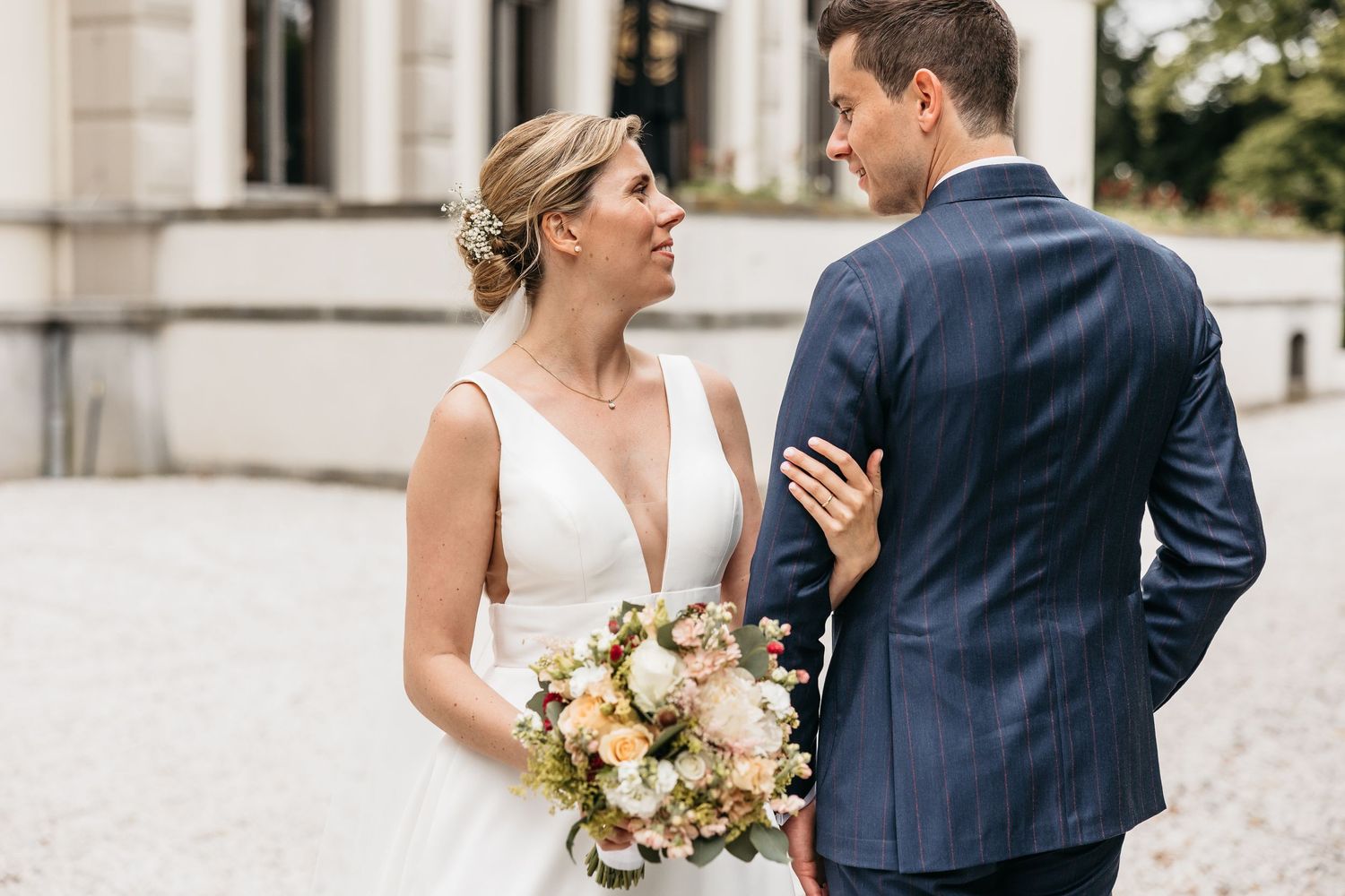 Bride with bouquet and groom in navy suit sharing an intimate glance at wedding venue.