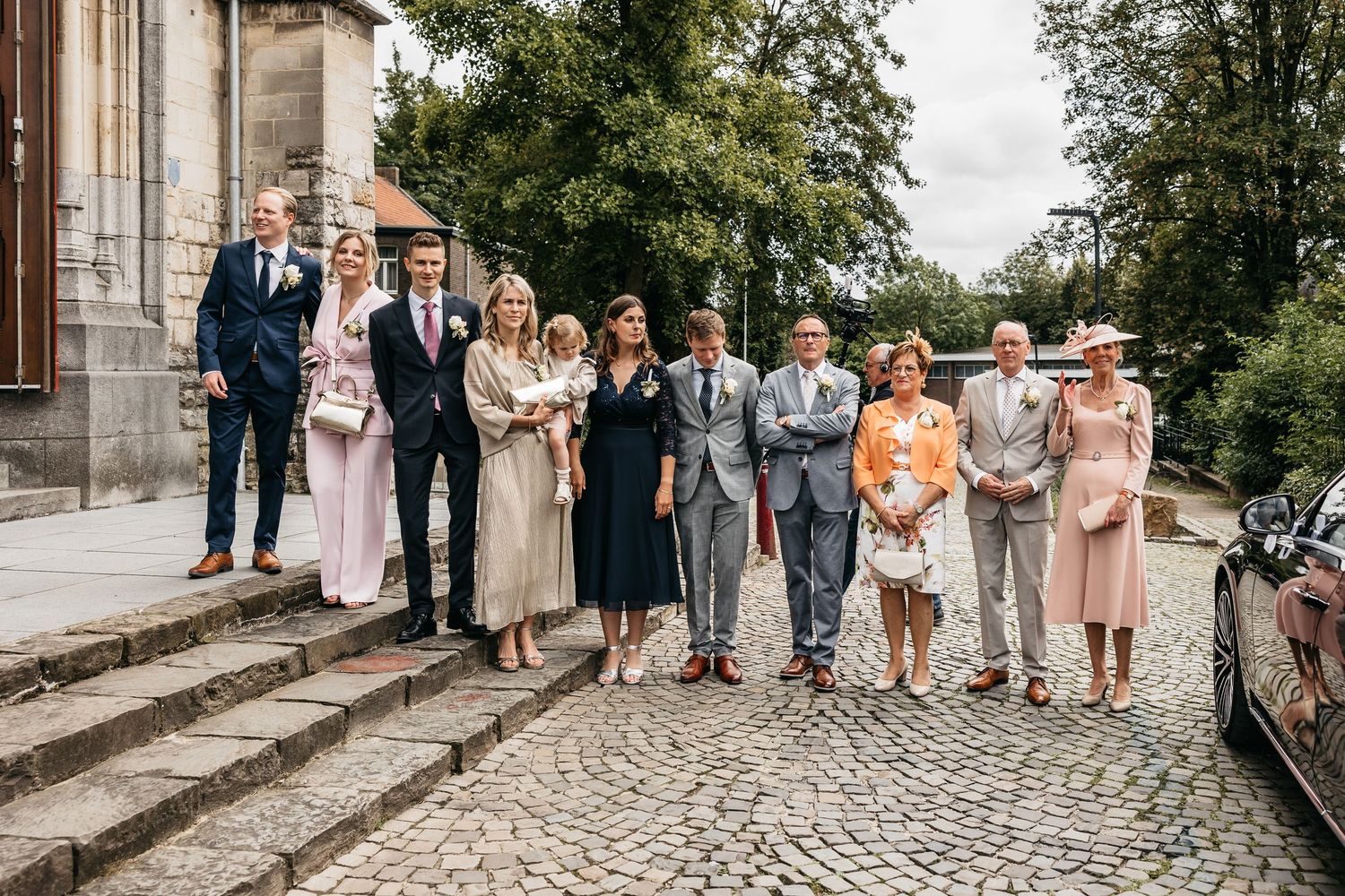 Wedding party group photo with nine guests posing on cobblestone steps outside a historic church.