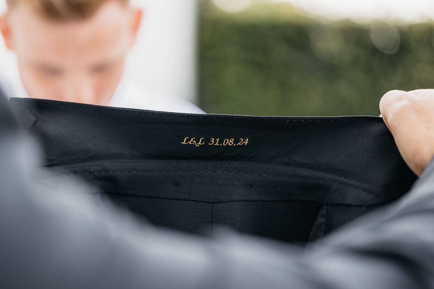 Close-up of a black suit jacket lining embroidered with initials and date 31.08.24.