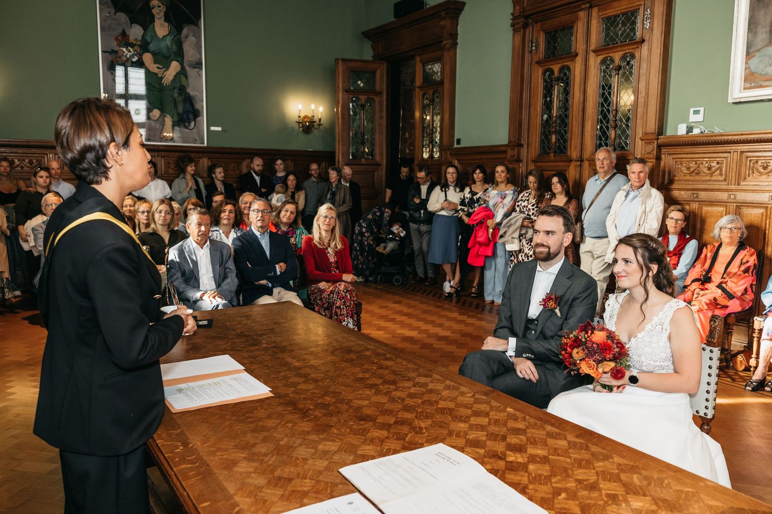 Bride and groom smile at officiant during intimate civil wedding ceremony with guests seated behind them.