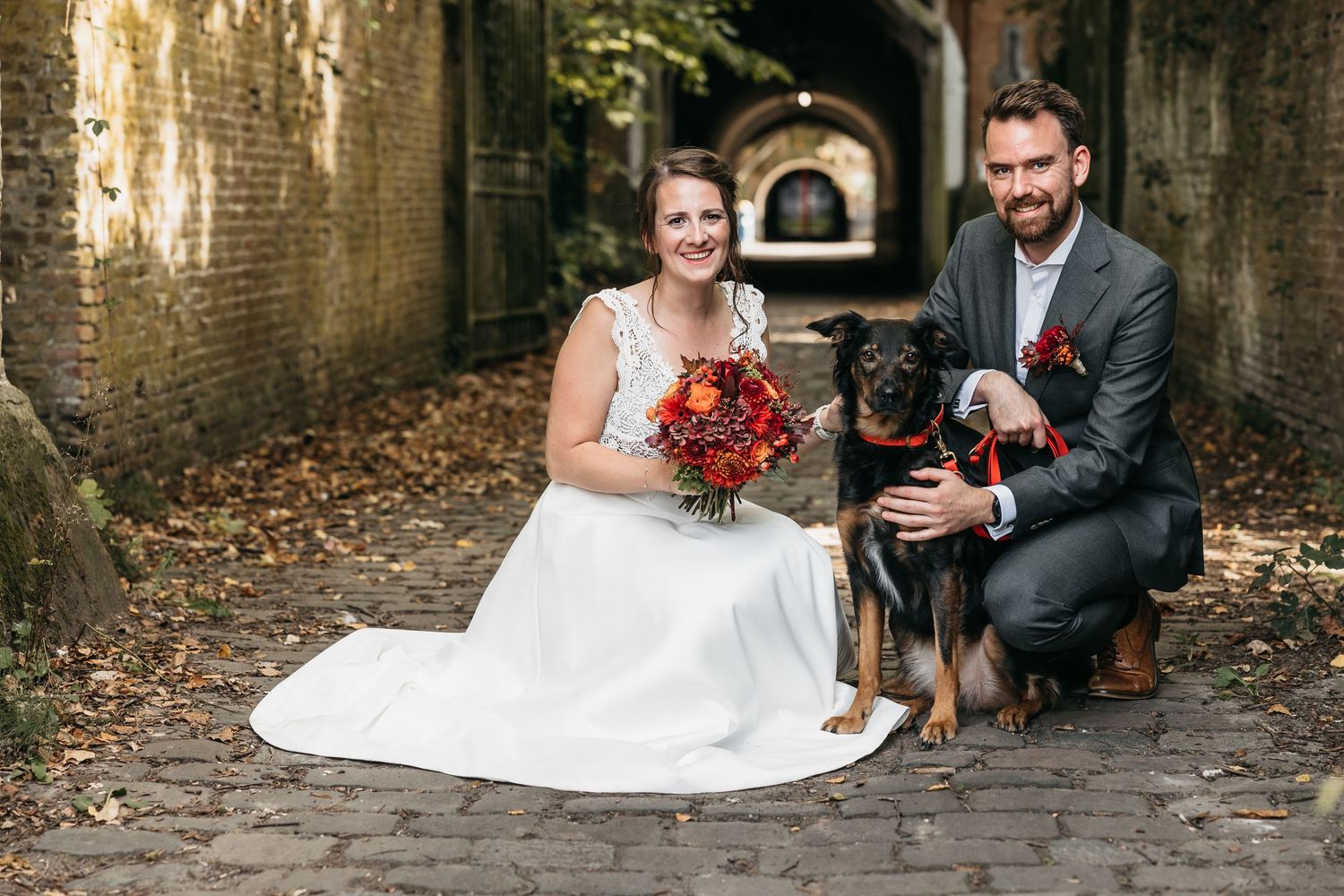 Bride and groom posing with their German Shepherd dog in a rustic brick archway on their wedding day.