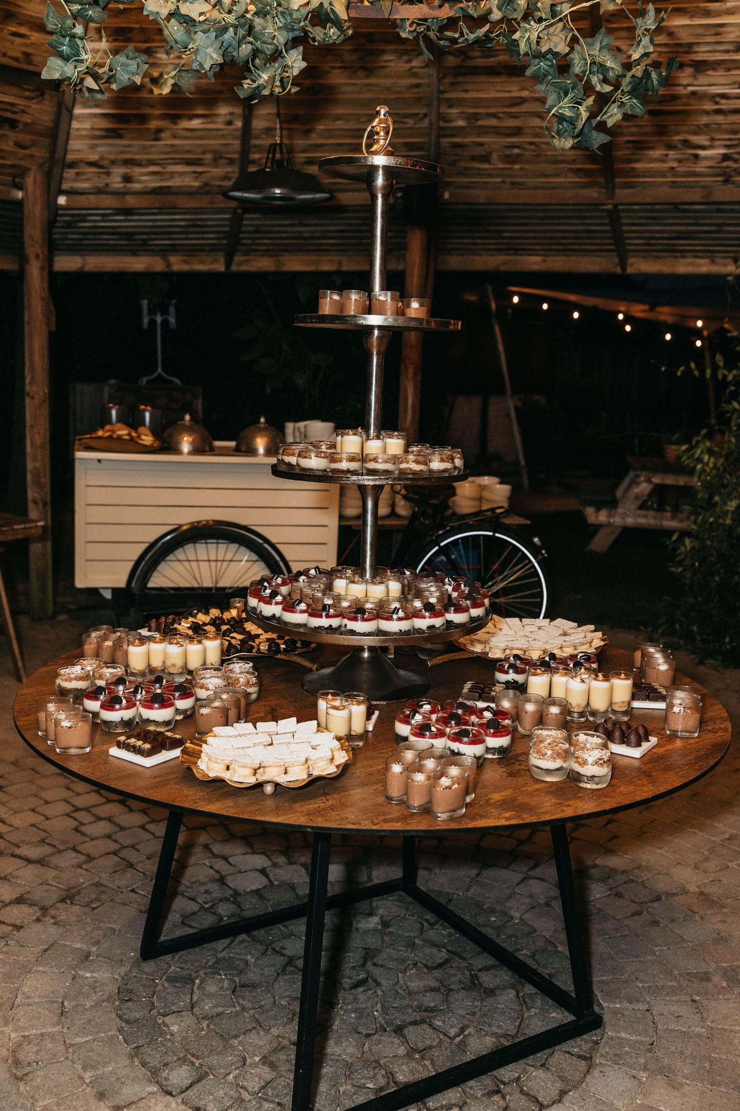 Elegant rustic wedding dessert table with tiered display and assorted sweet treats at night.