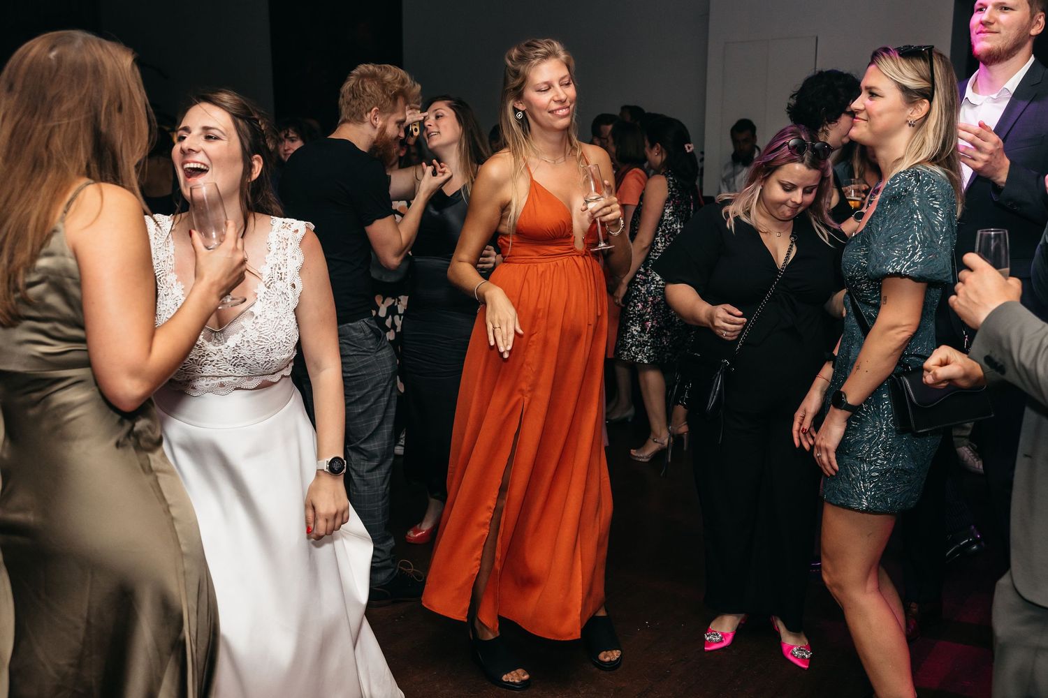 Bride and guests laugh and dance together on crowded wedding reception dance floor.