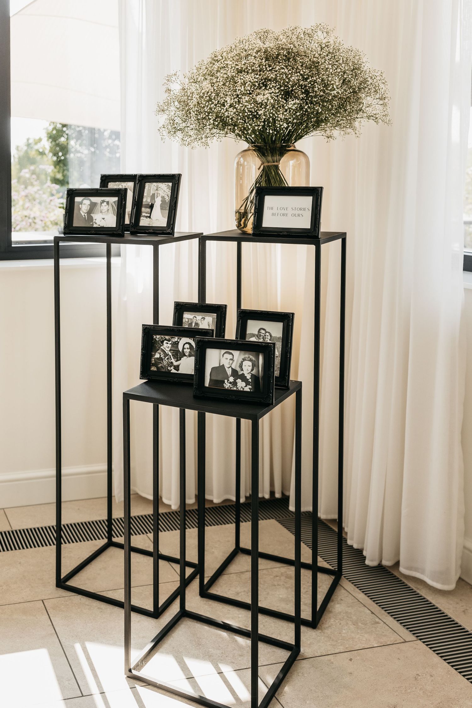 Black metal display stands with framed black and white photos and baby's breath floral arrangement.