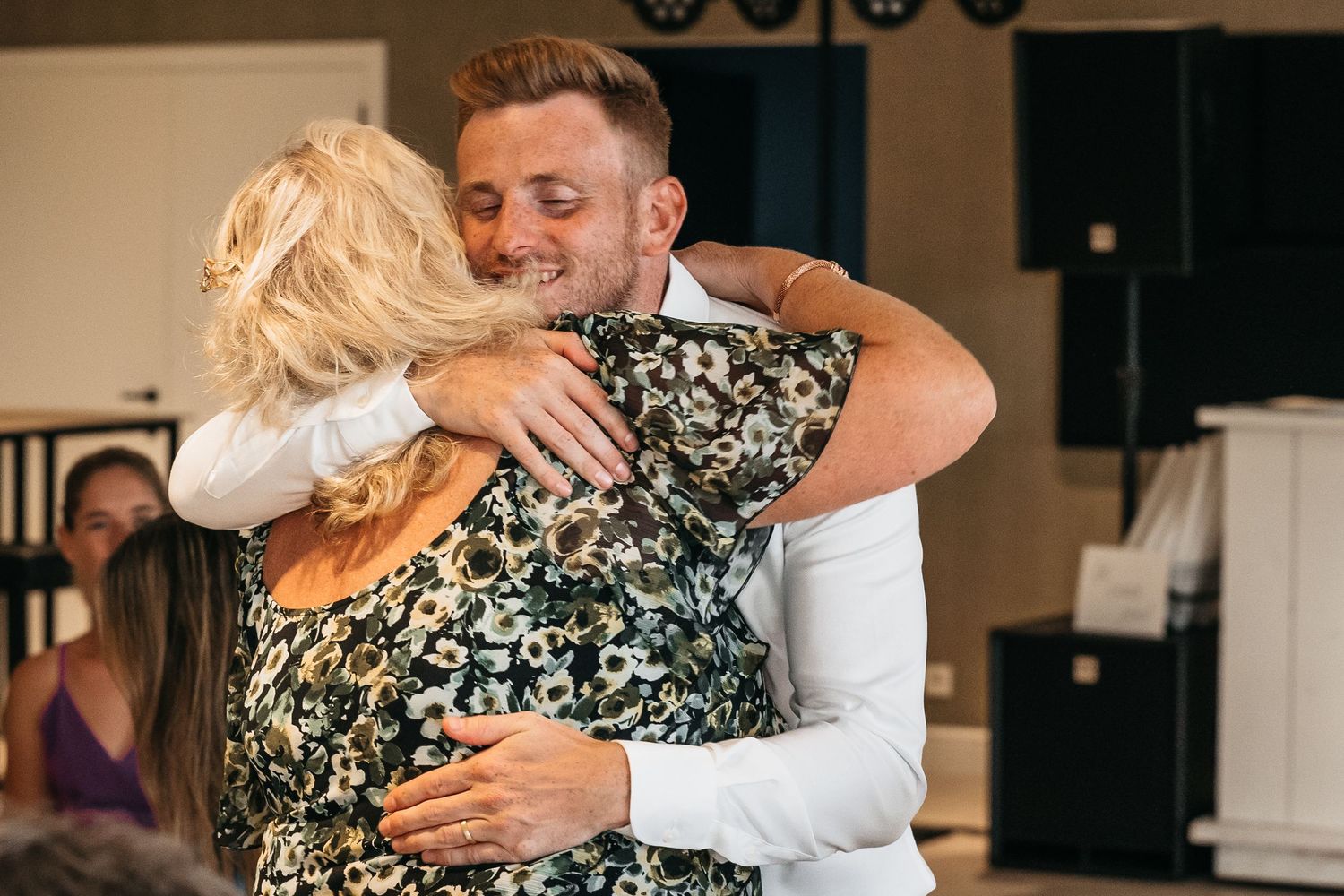 Groom sharing a warm embrace with an older woman in a floral dress at the wedding reception.