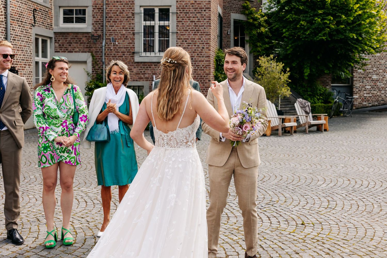Groom smiling as bride in white gown approaches during first look outdoors.