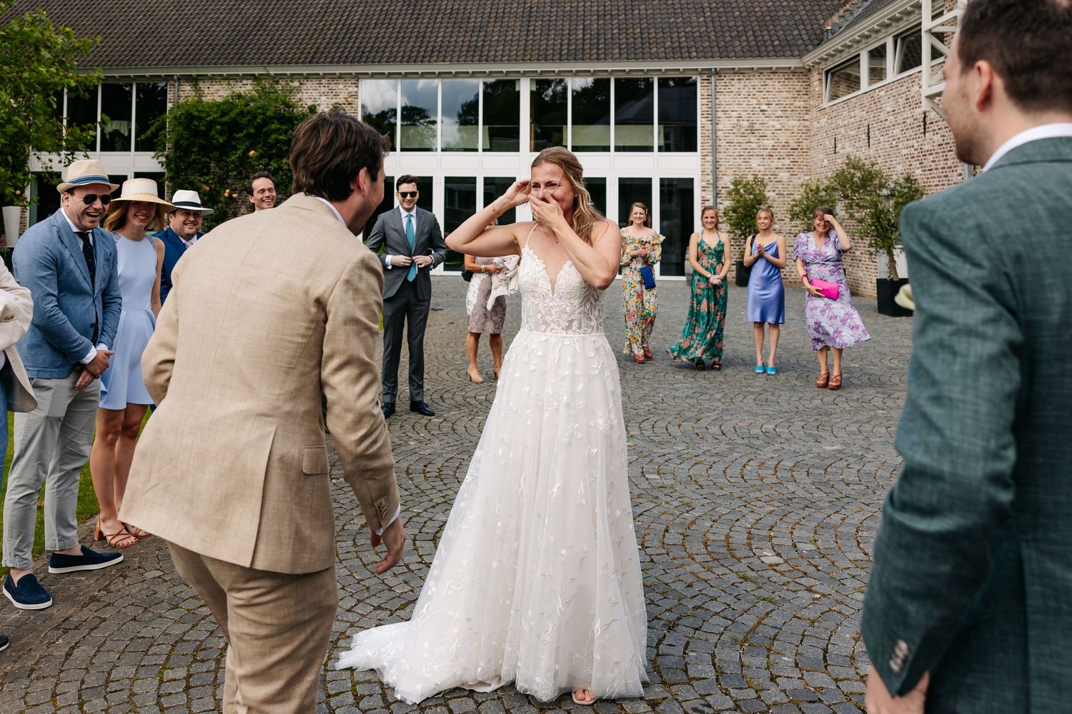 Bride in white lace gown reacting with surprise during outdoor wedding first look moment.