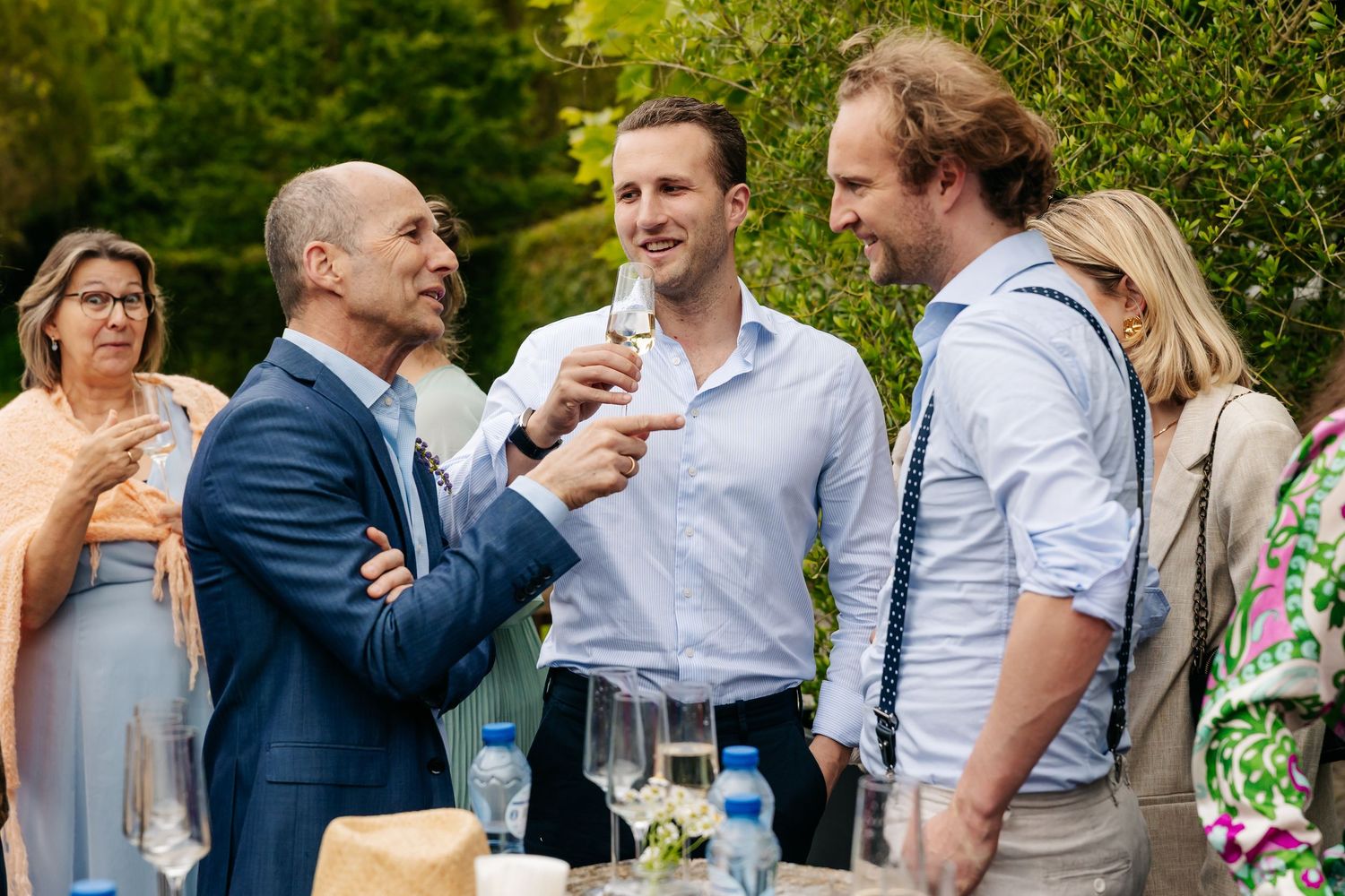 Guests in formal attire socializing and toasting with champagne at outdoor wedding reception.