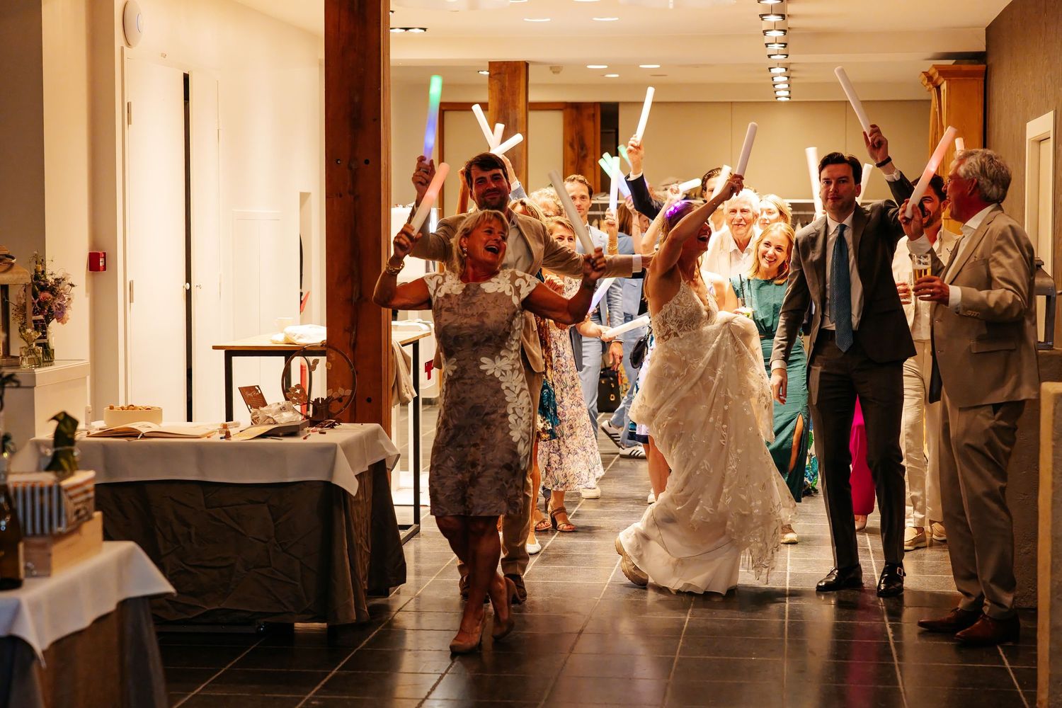 Bride and groom entering wedding reception with guests holding glowing foam sticks.