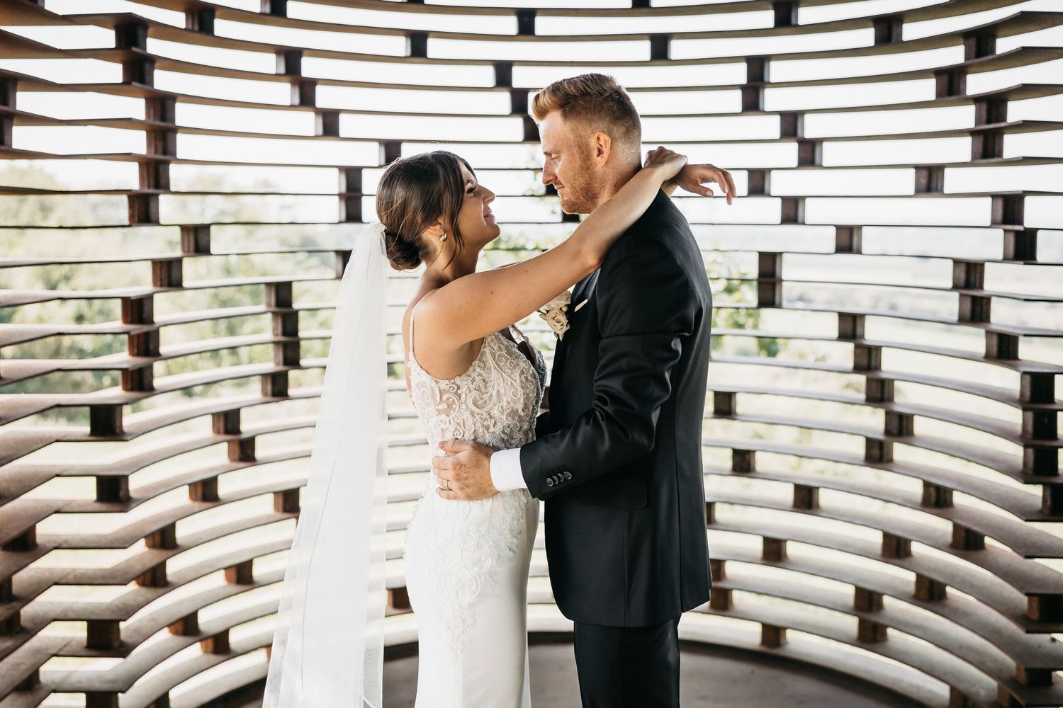 Bride and groom share a joyful embrace inside a curved wooden lattice chapel interior on their wedding day.