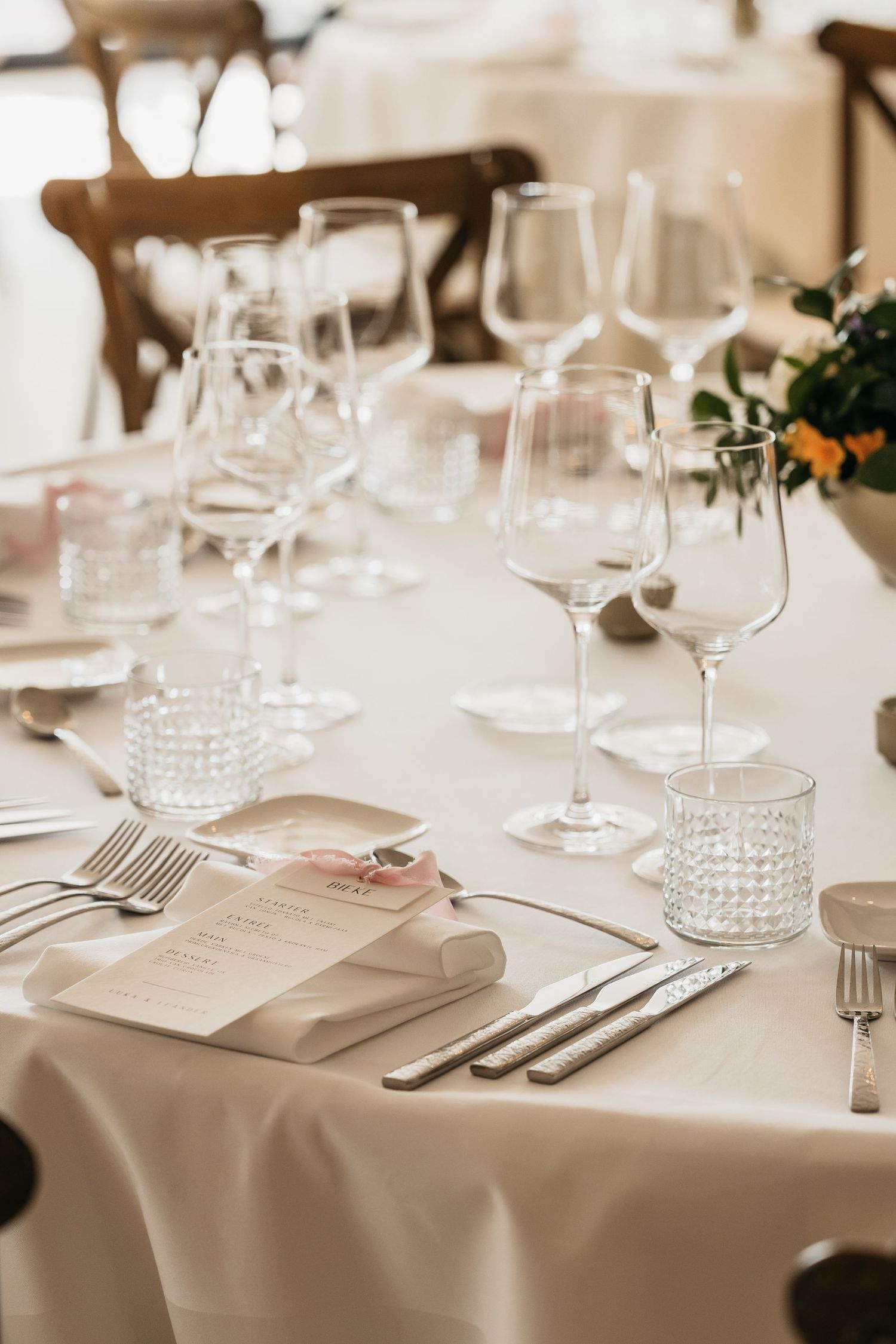 Elegant wedding table setting with white linen, crystal glassware, silver cutlery, and menu cards.