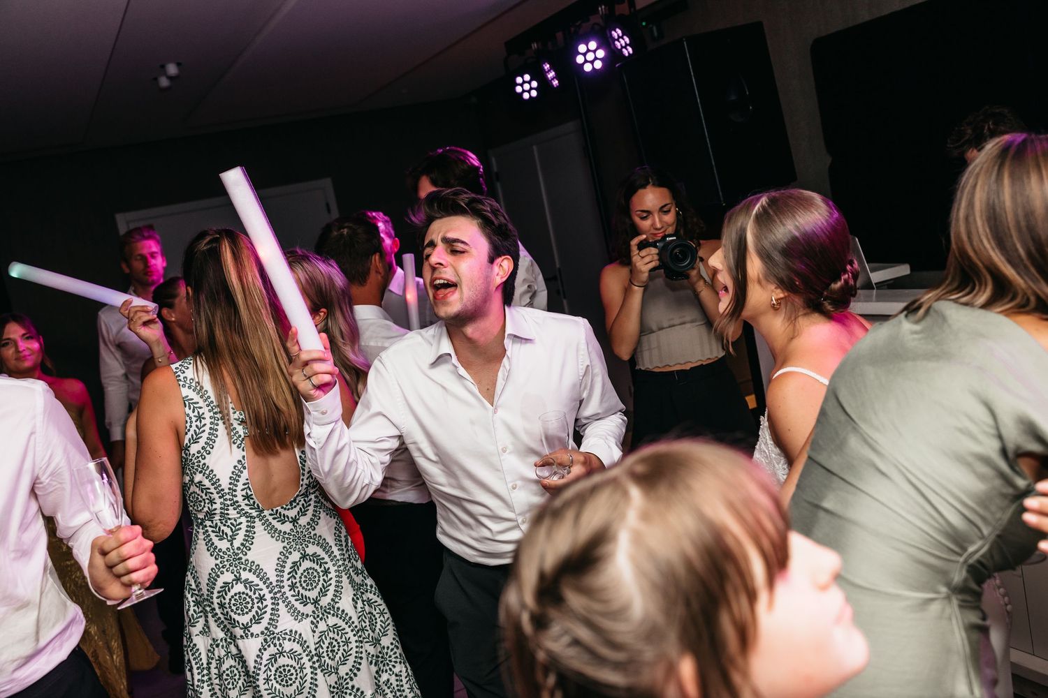 Joyful wedding guest in white shirt dances energetically with others at lively reception party.