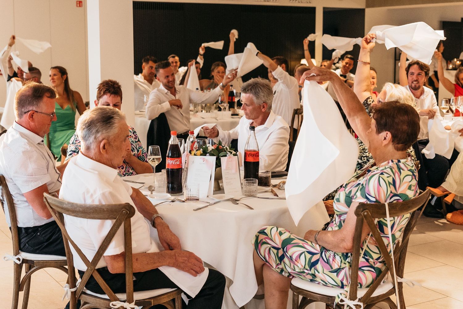 Wedding guests waving white napkins in celebration at reception dinner.