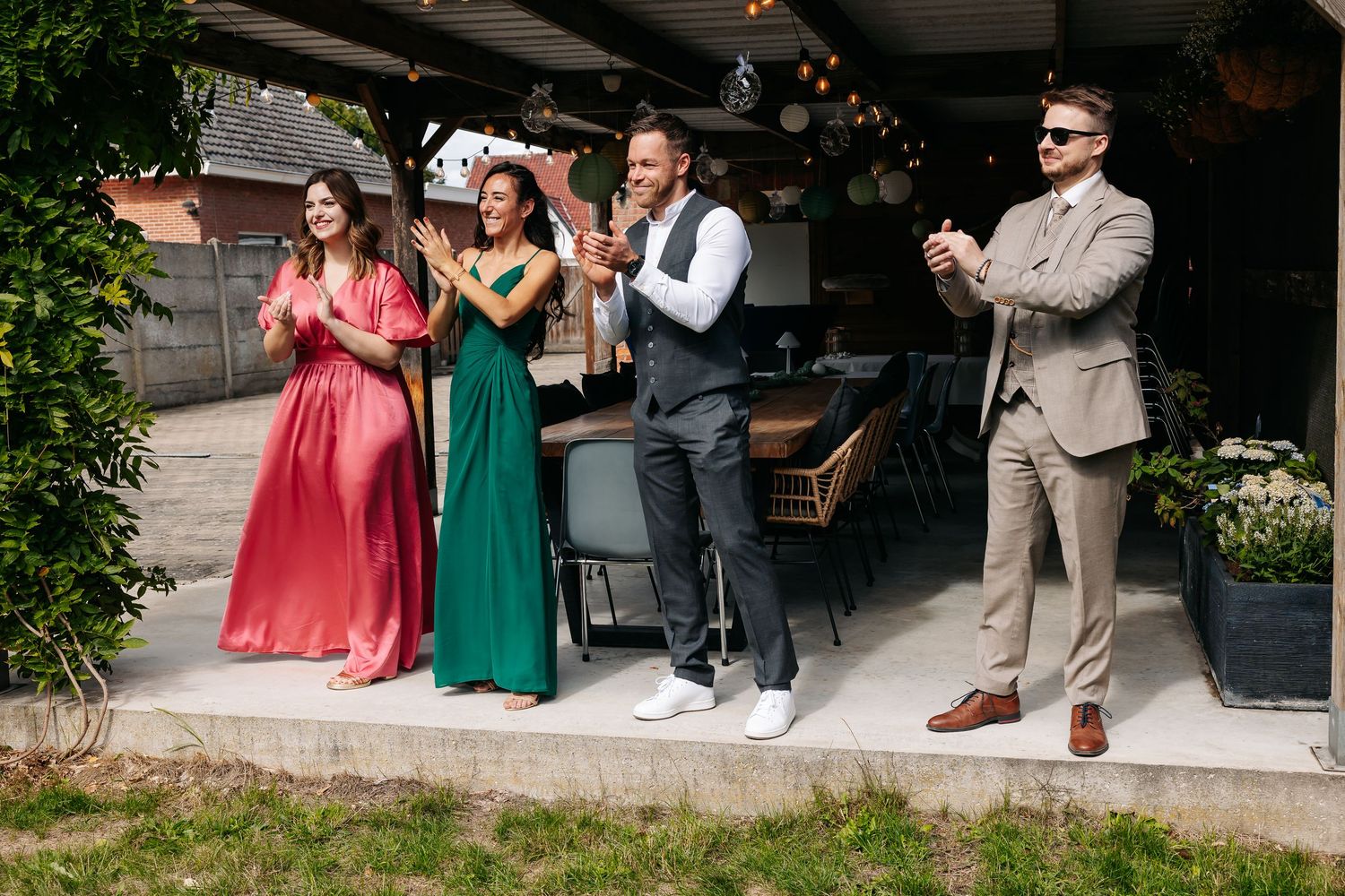 Wedding guests clap and celebrate outdoors at rustic venue with string lights.
