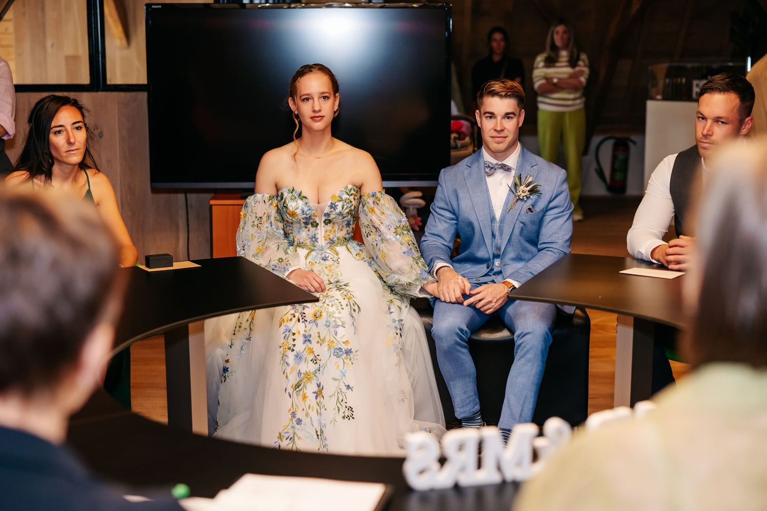 Bride and groom seated at table during wedding ceremony in rustic indoor venue.