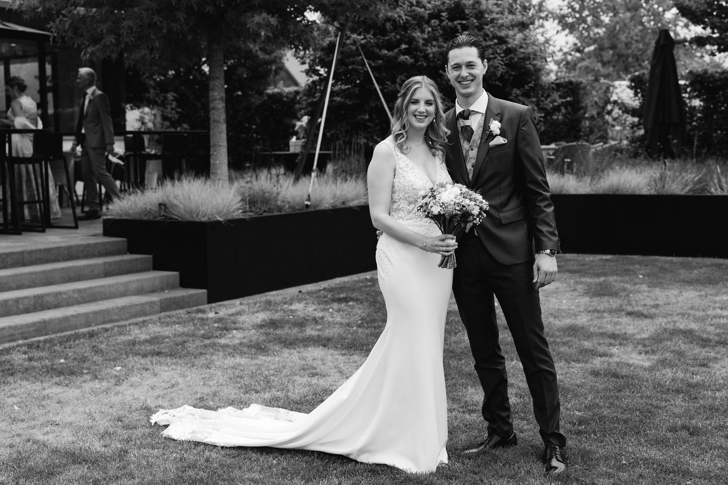 Classic black and white wedding portrait of bride and groom standing together on lawn outside elegant venue.