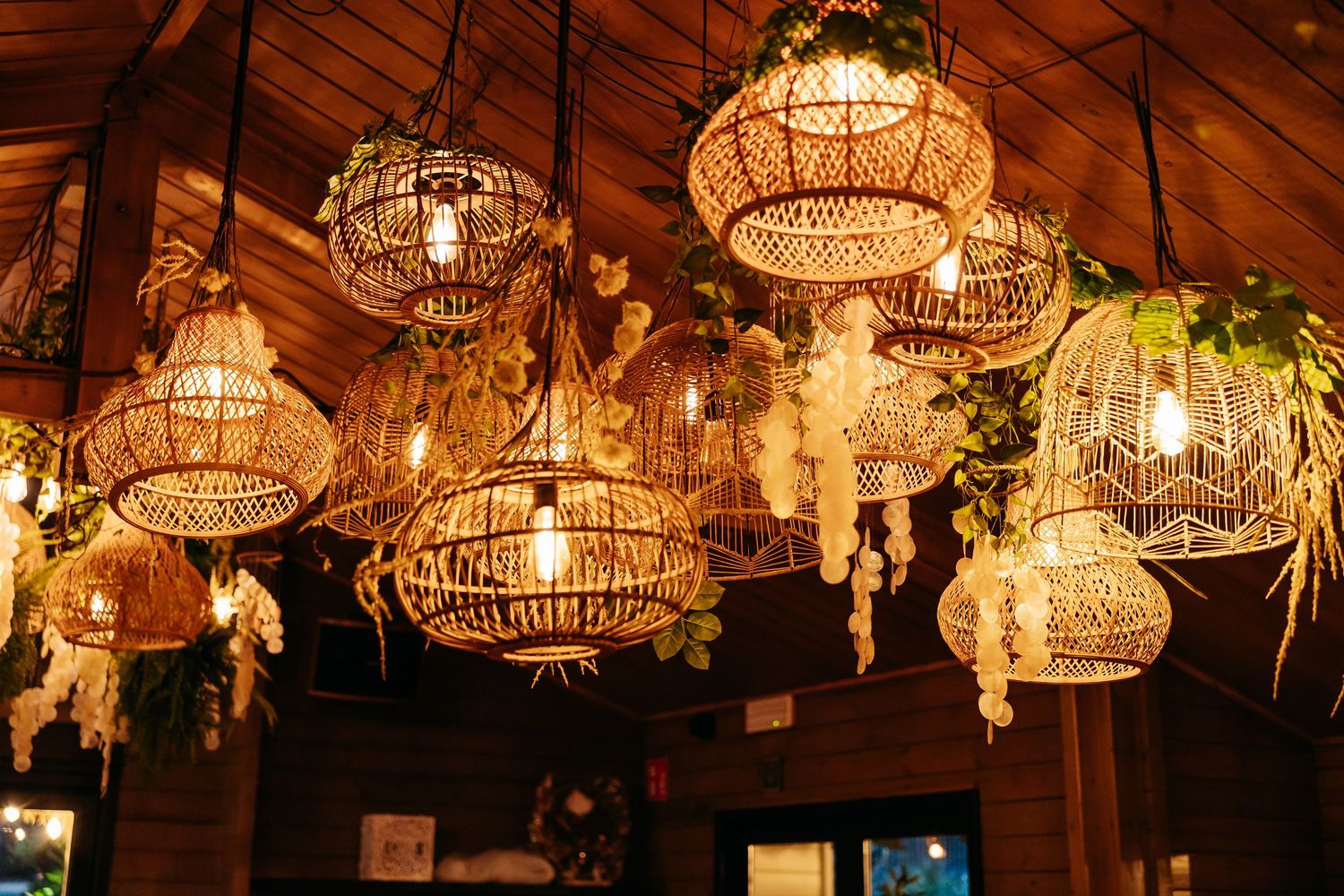 Warm boho restaurant ceiling decorated with wicker pendant lights and hanging greenery creating cozy ambiance.