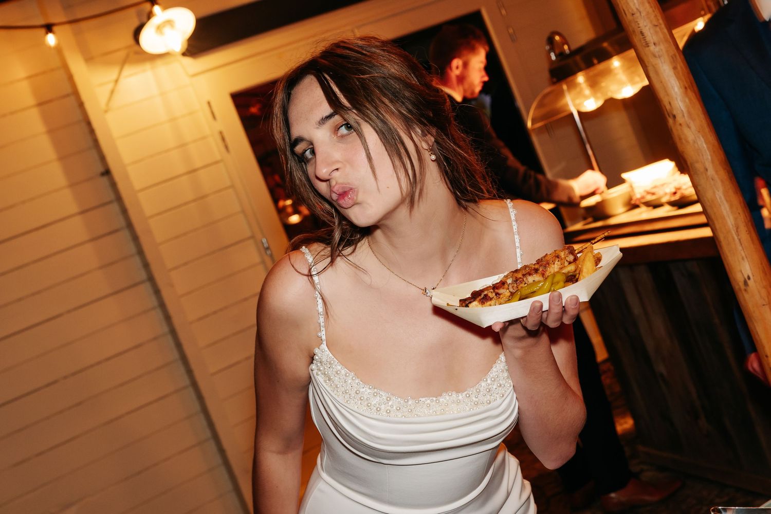 Young woman in white dress holding a plate of food at a wedding reception.