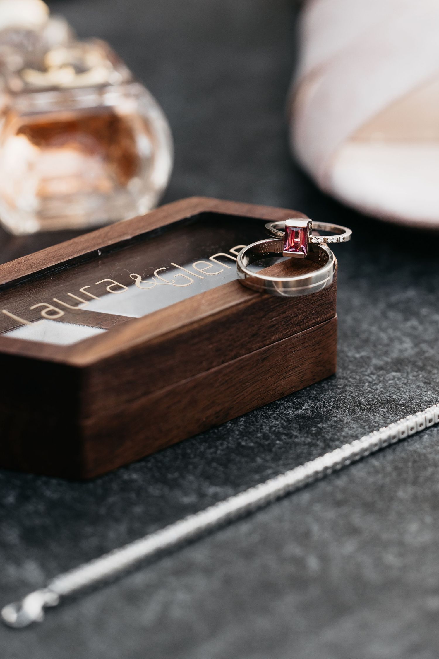 Wedding rings and band displayed on a personalized wooden box with Laura name engraving, beside perfume and bridal heels.