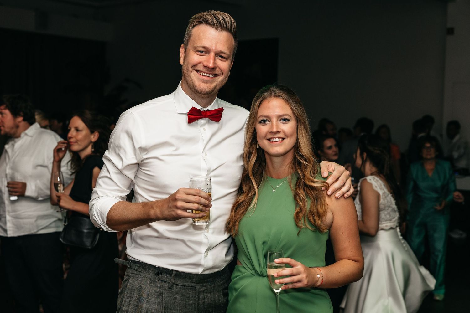 Smiling couple poses together at wedding reception, man wearing red bow tie.