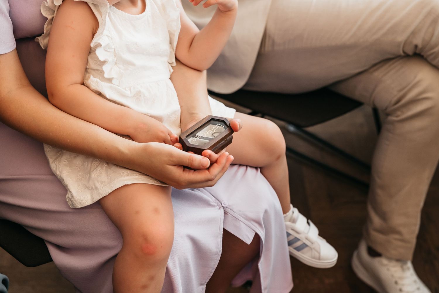 Child sits on adult lap holding a small device during a wedding ceremony indoors.