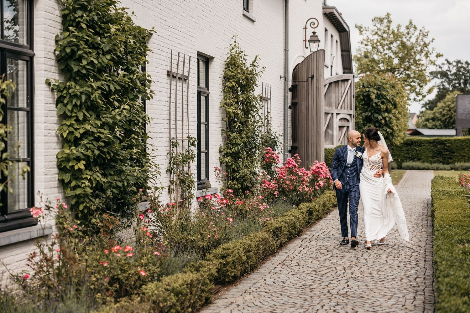 Bride and groom walking hand in hand along a cobblestone path with blooming roses.