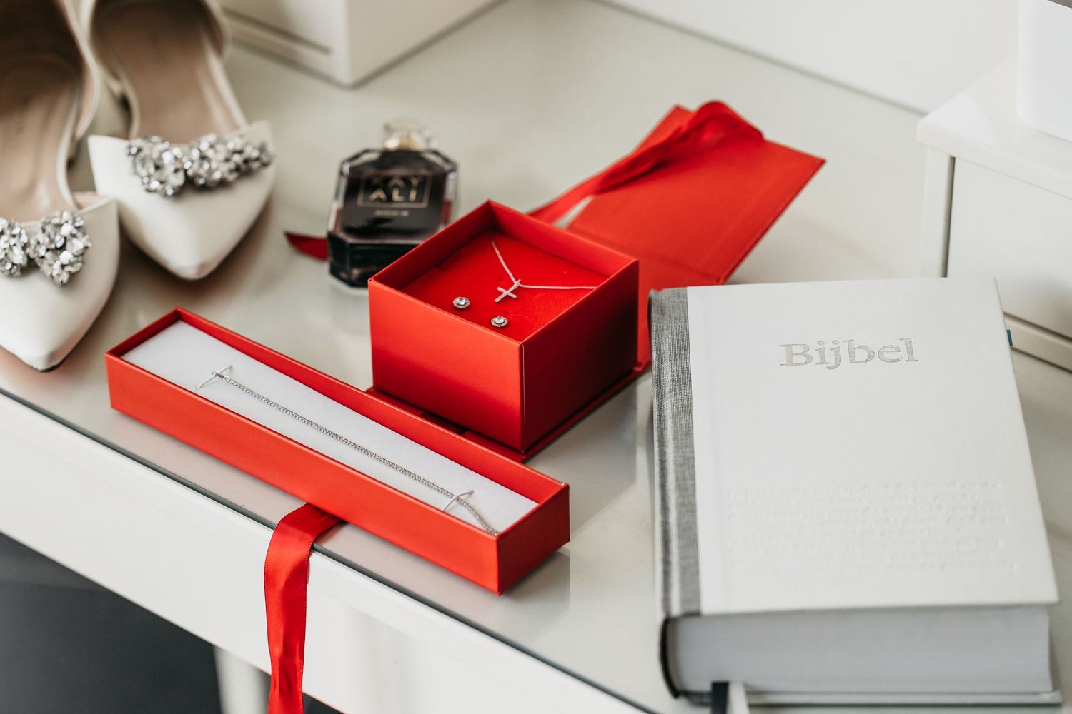 Bridal accessories flat lay with jewelry boxes, Bijbel book, and crystal embellished shoe.