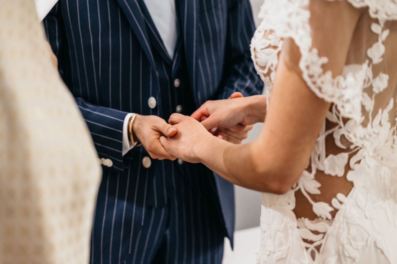 Close-up of bride placing wedding ring on grooms finger during marriage ceremony.