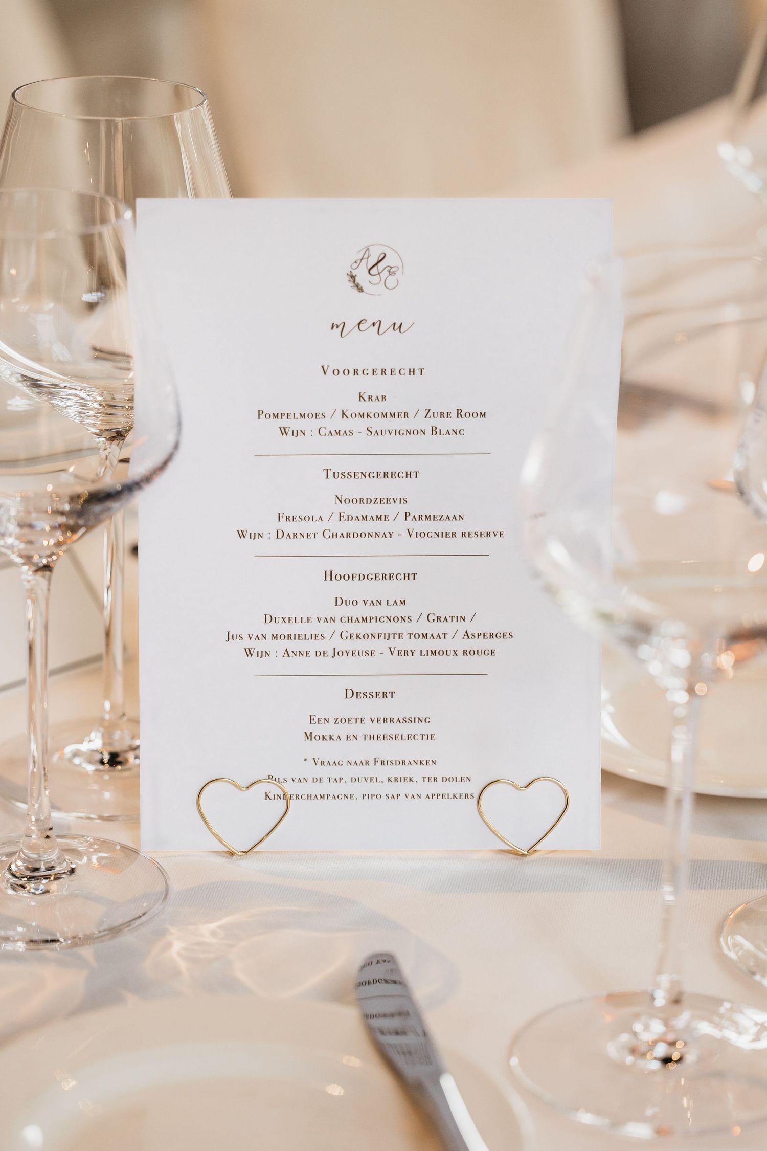 Elegant wedding menu card with gold heart details displayed between crystal wine glasses on a white table.