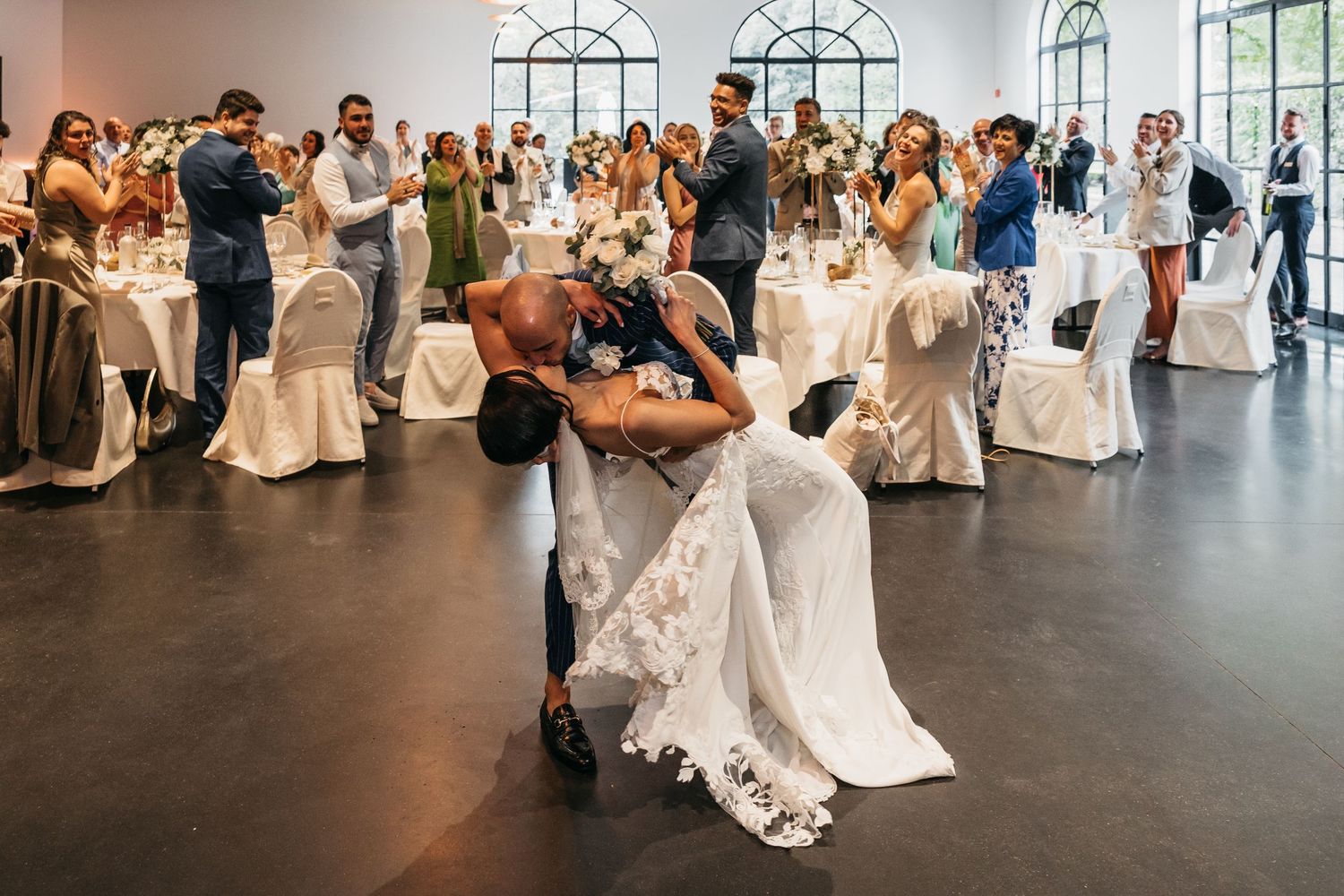 Groom dips bride in stunning white lace wedding gown during romantic first dance at elegant reception.