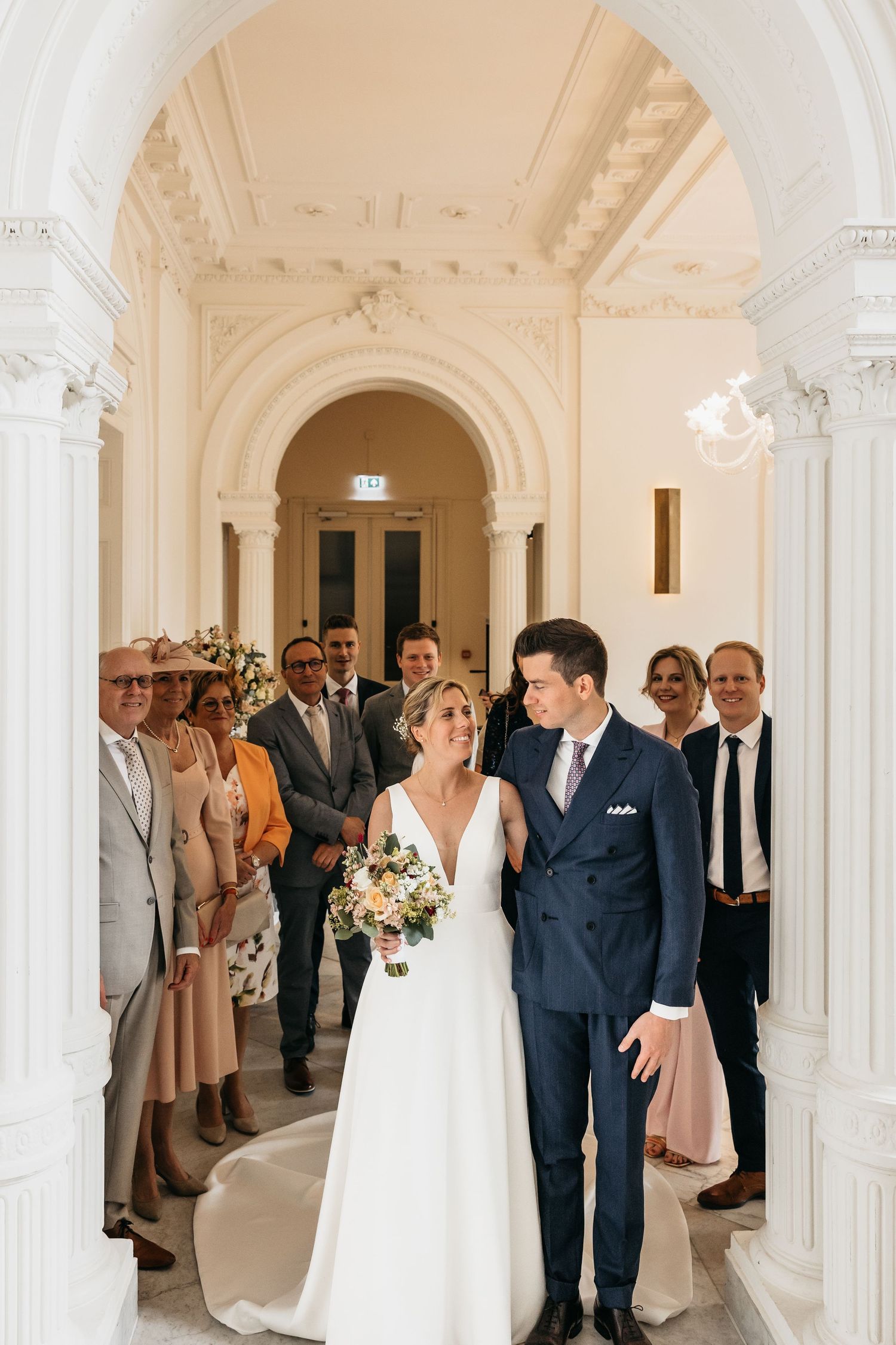 Bride and groom walk through ornate archway surrounded by smiling wedding guests.