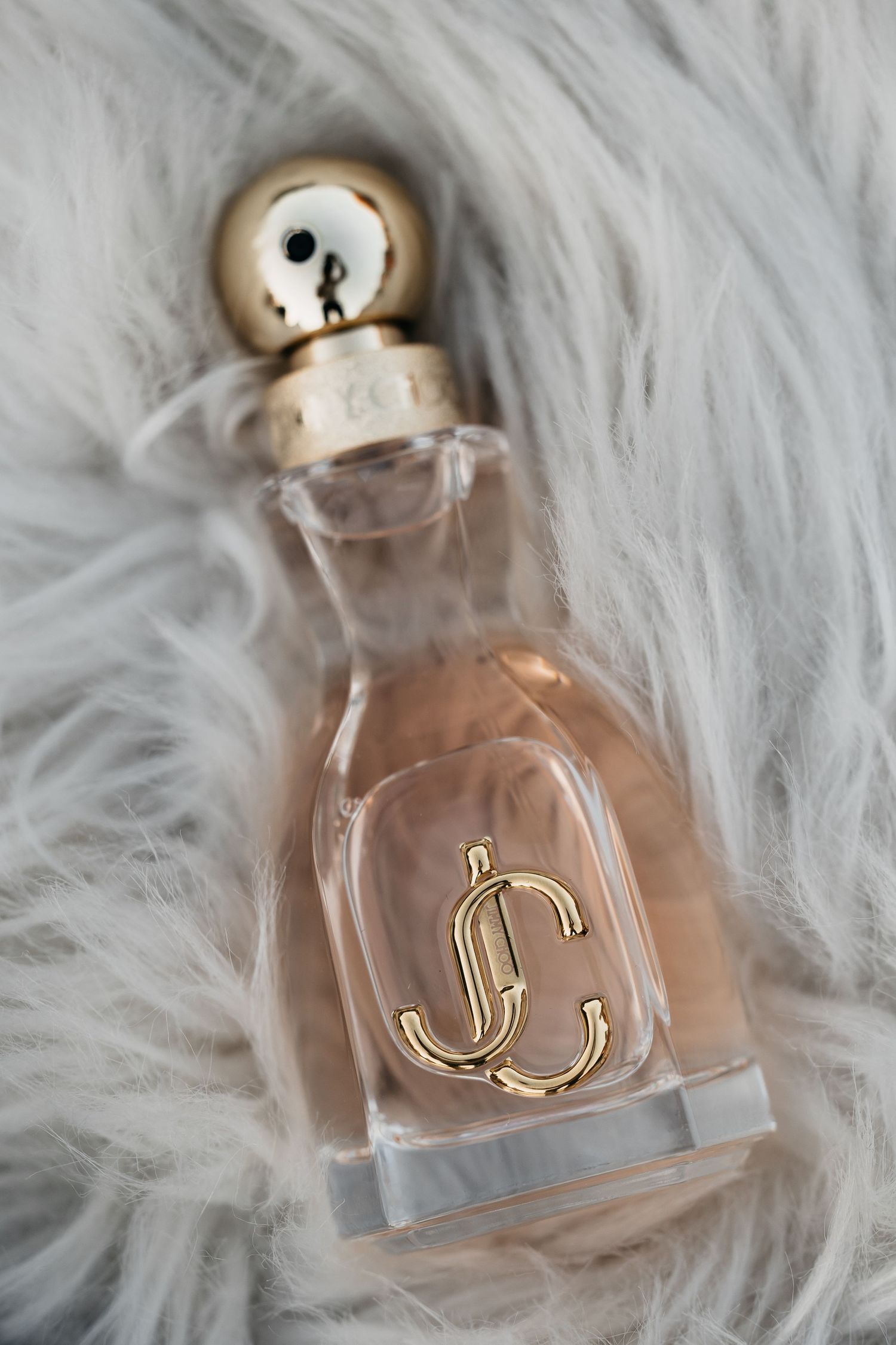 Jimmy Choo perfume bottle with gold cap resting on a white fluffy fur surface.