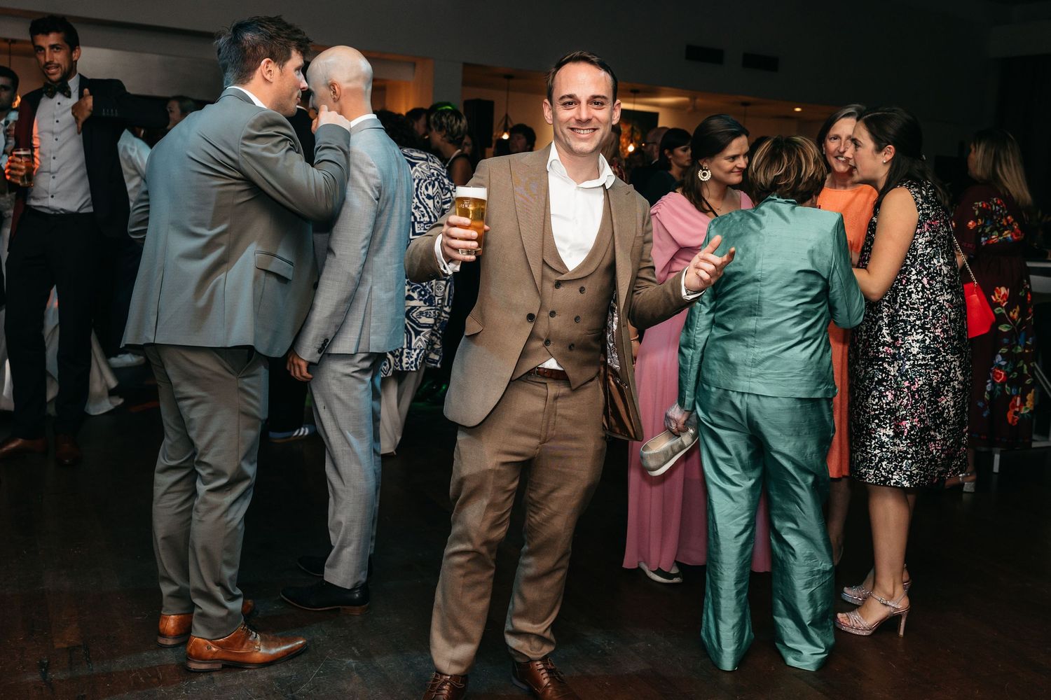 Smiling man in tan suit holding beer at wedding reception party.