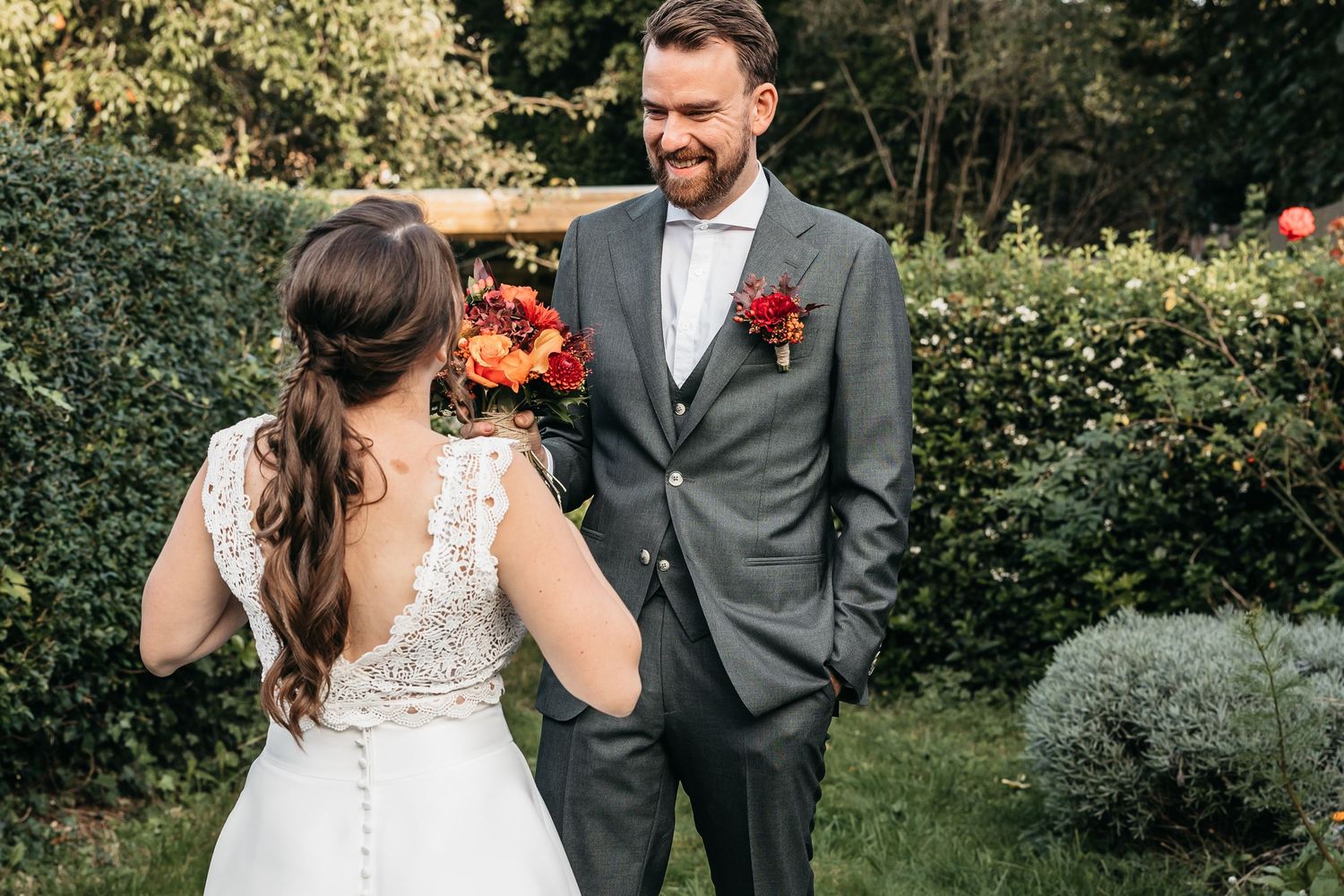 Bride and groom sharing a smile during their first look in a lush green garden setting.
