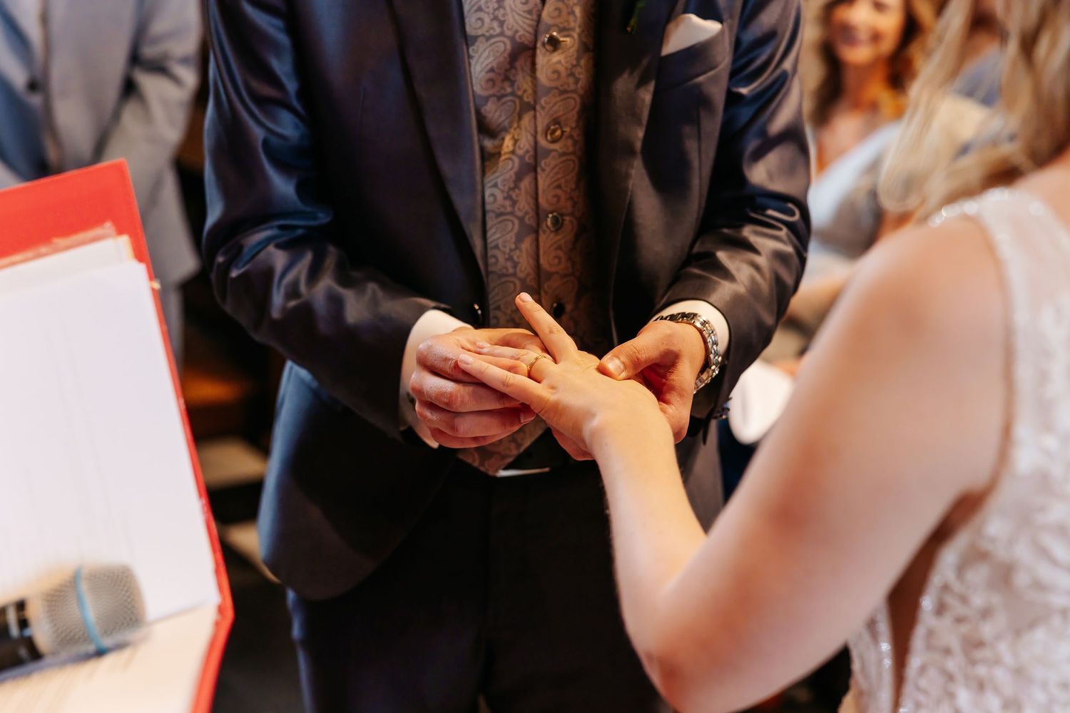 Groom placing wedding ring on bride's finger during church ceremony.