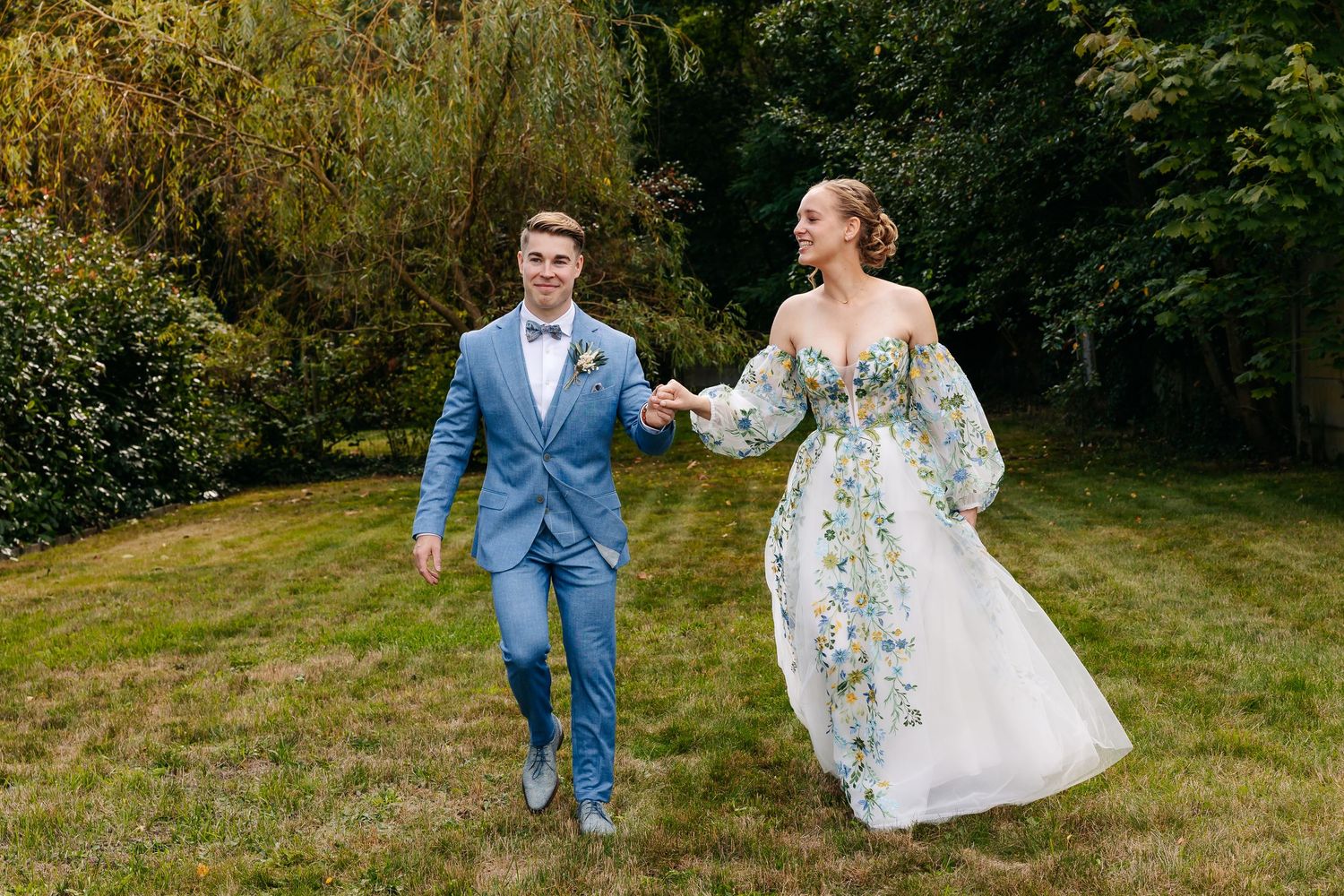 Happy bride and groom walk hand in hand through lush green garden on wedding day.