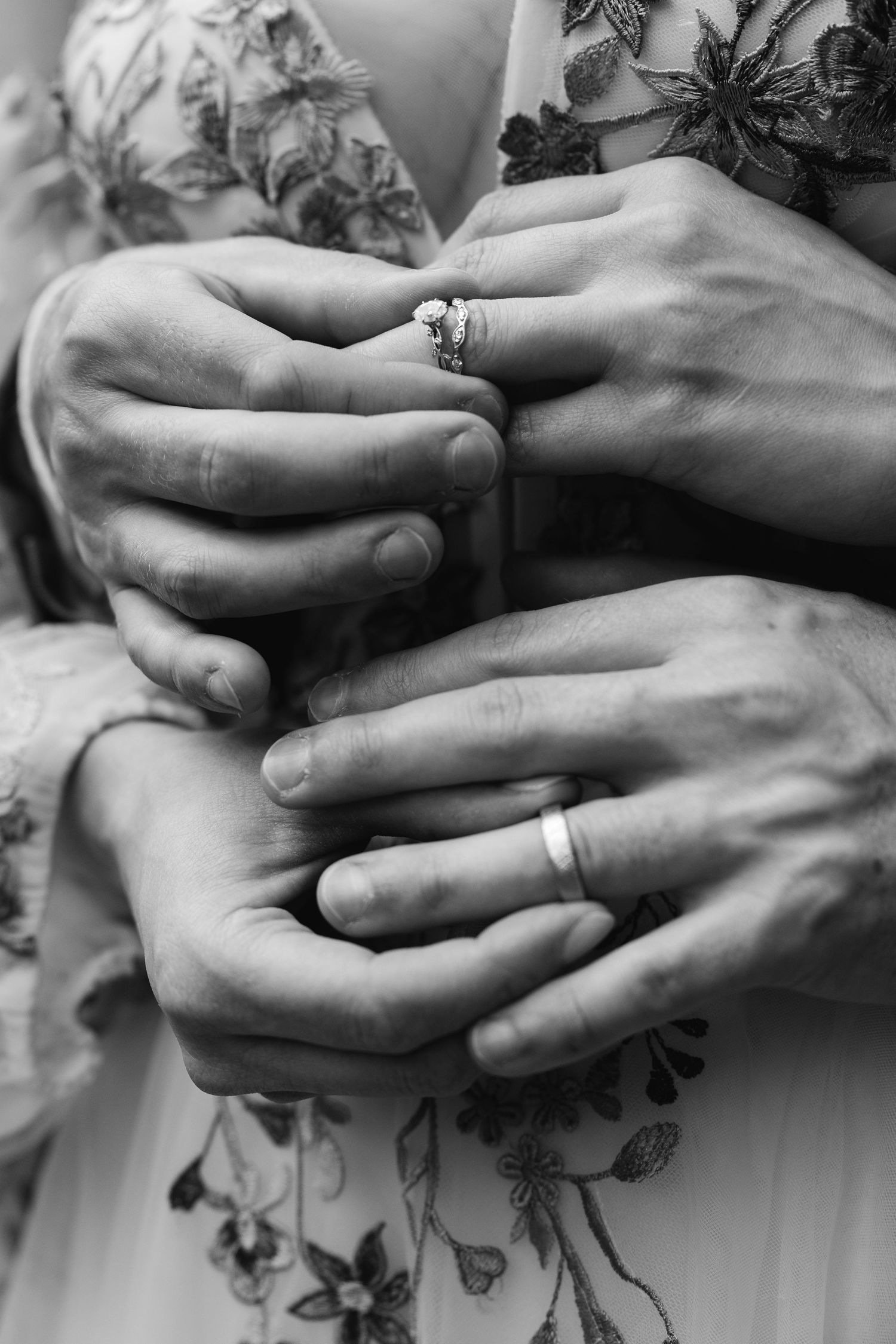 Black and white photo of bride and groom holding hands showing wedding rings.