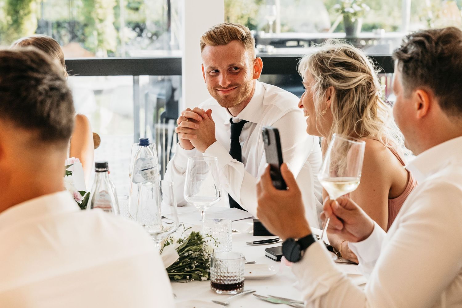 Wedding guest smiling and chatting while holding a wine glass at the reception table.
