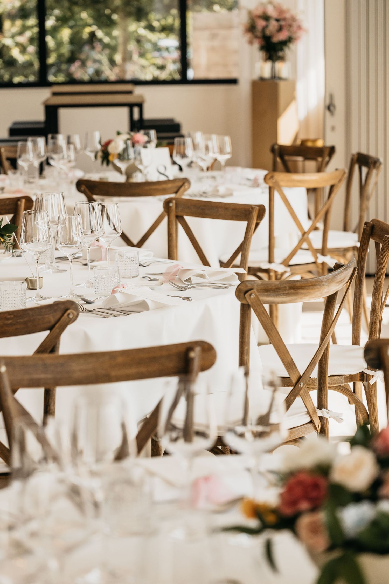 Elegant wedding reception with wooden cross-back chairs and white linen tables set with crystal glassware.
