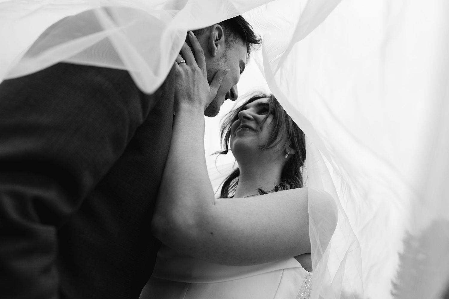 Intimate black and white wedding photo of couple sharing a tender moment under the bridal veil.