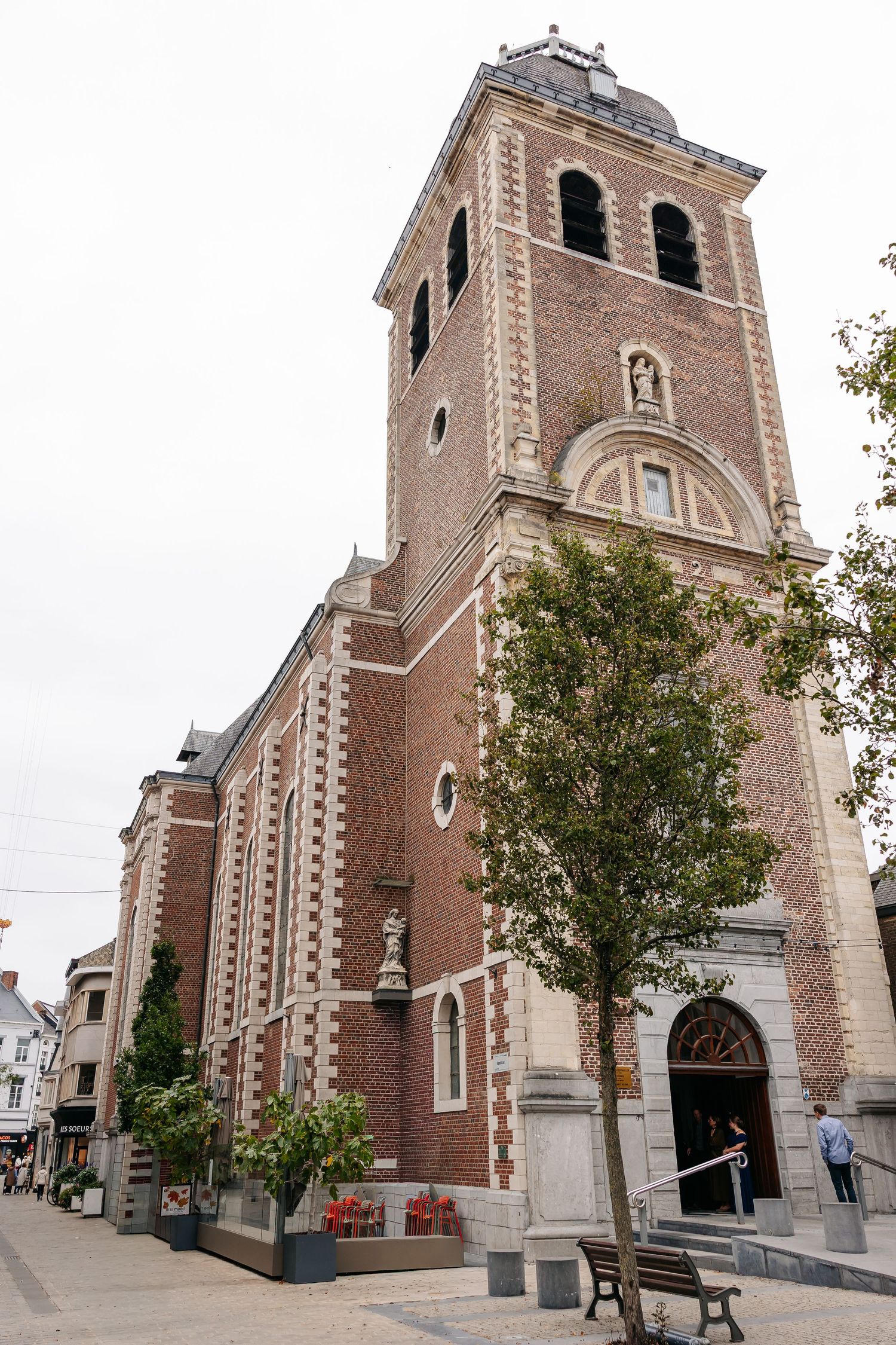 Brick church tower of Virga-Jessebasiliek in Hasselt, Belgium, with trees lining the pedestrian street.