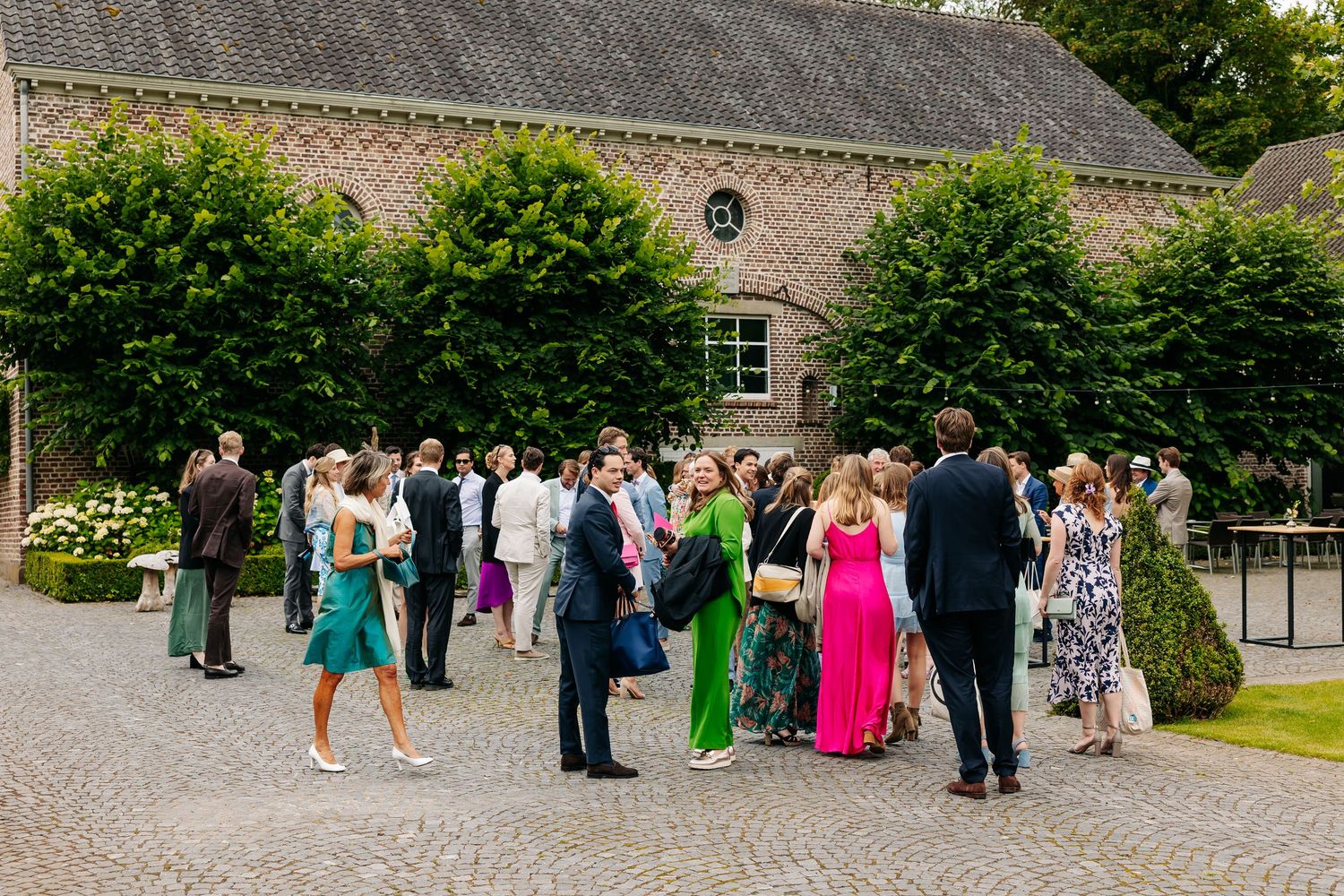 Wedding guests mingling outdoors in colorful attire at an elegant brick estate venue.