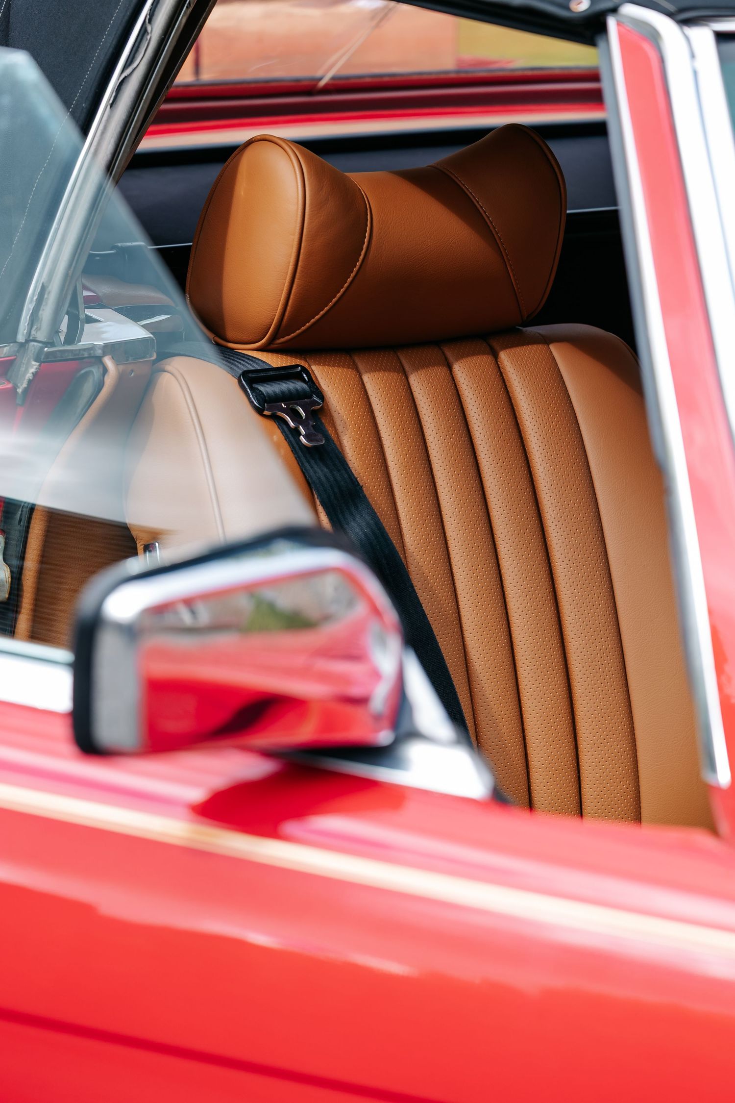 Close-up of tan leather interior seat with headrest and seatbelt in a classic red vintage car.