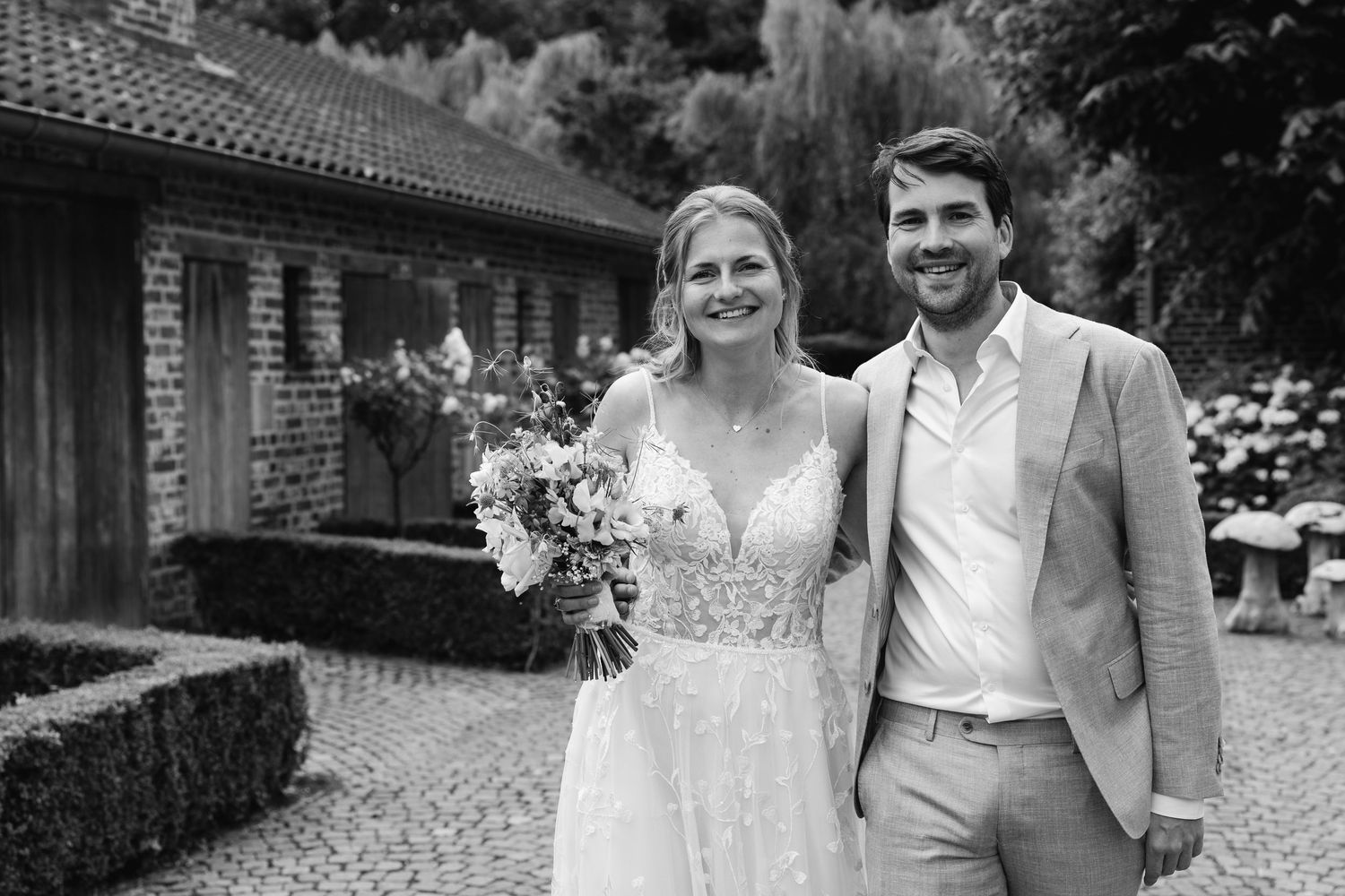 Black and white photo of smiling bride and groom posing outside rustic stone wedding venue.