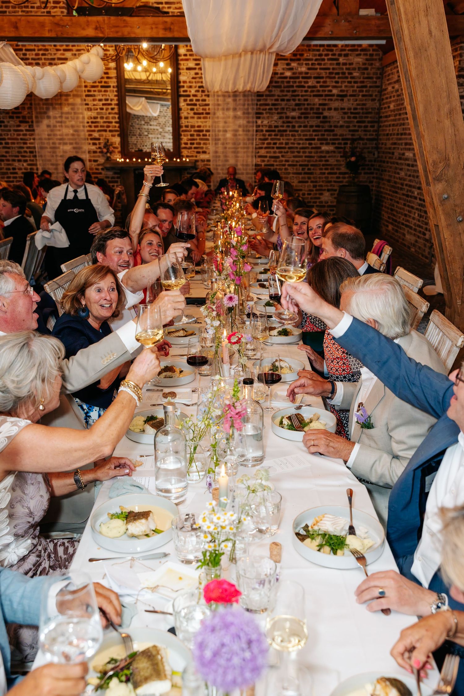 Wedding guests raising glasses in a toast at a long decorated dinner table.