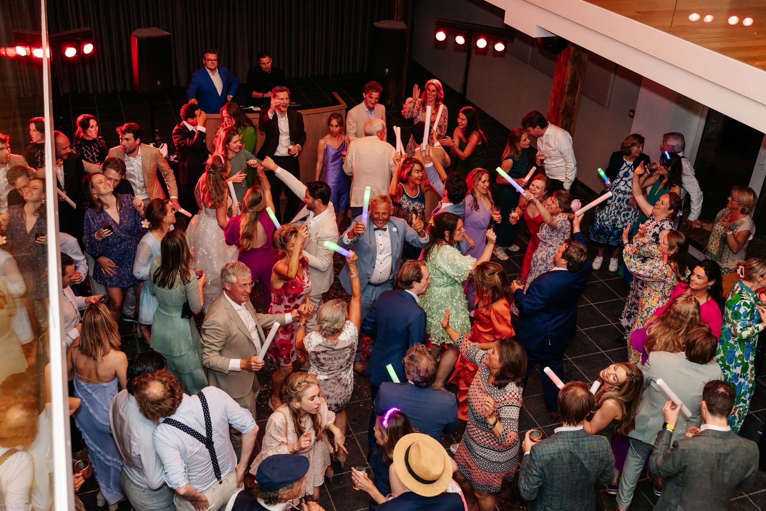 Aerial view of crowded wedding dance floor with colorful guests dancing under stage lights.