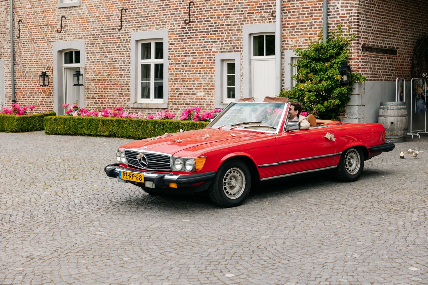 Classic red Mercedes-Benz SL convertible parked on cobblestone courtyard outside brick building.